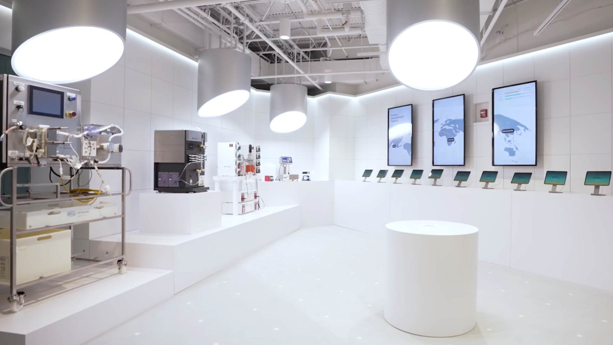 A frame from the Stellix Customer Engagement Center video - an all-white technology exhibit space displaying various industrial and scientific equipment, digital screens, and informational displays.