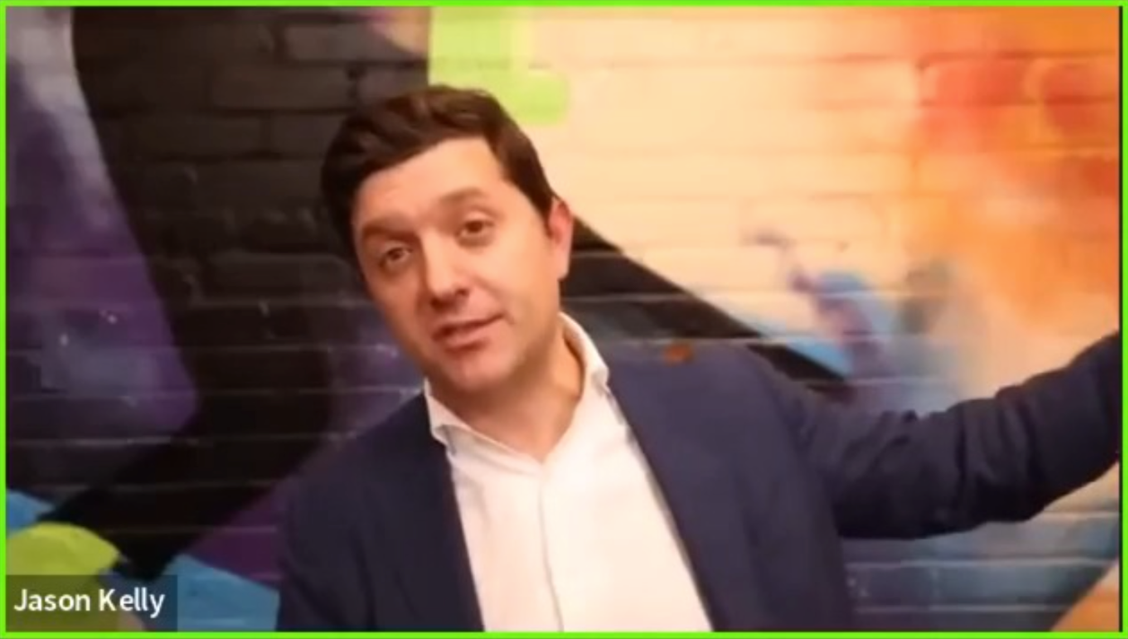 A frame from the Ginkgo Bioworks Earnings Call Livestream - A man (CEO Jason Kelly) with brown hair in a white shirt and navy blazer seated in front of a colorful wall, on a Zoom call.