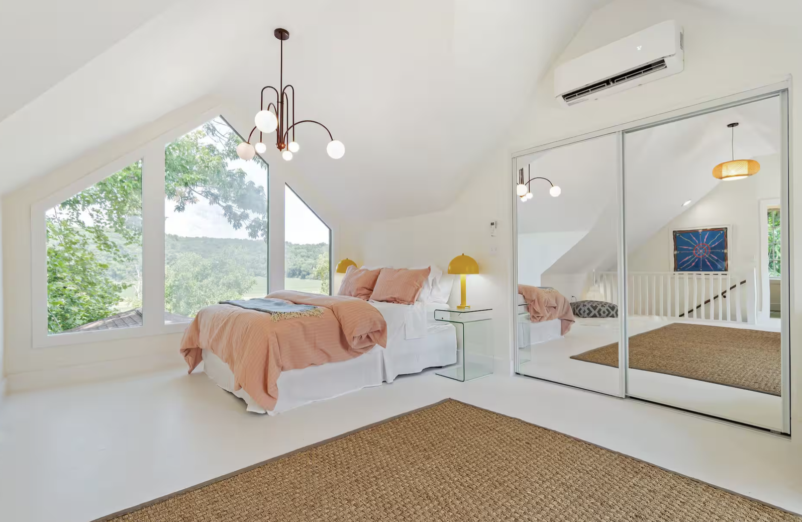 Bright bedroom with a peach-colored bed, large window with outdoor view, mirrored closet doors, and modern chandelier.