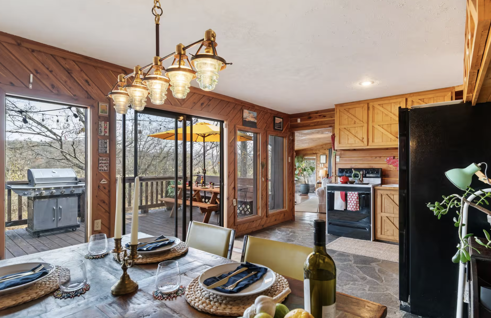 Interior of a wooden cabin kitchen and dining area with a view of an outdoor patio.