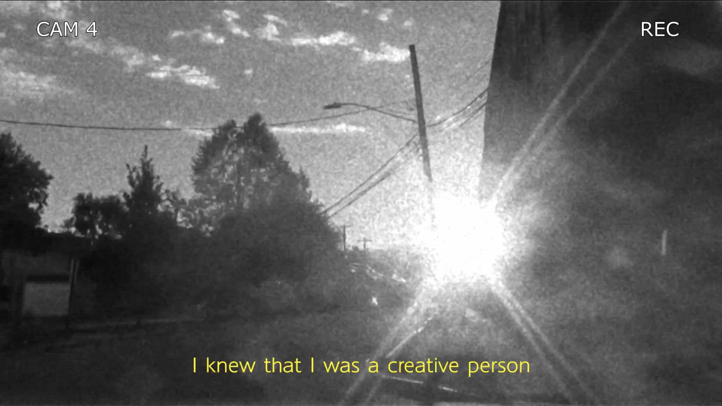 Black and white image of a street scene at night with power lines, trees, and a bright light at the horizon. Subtitles at the bottom say, 'I knew that I was a creative person.'