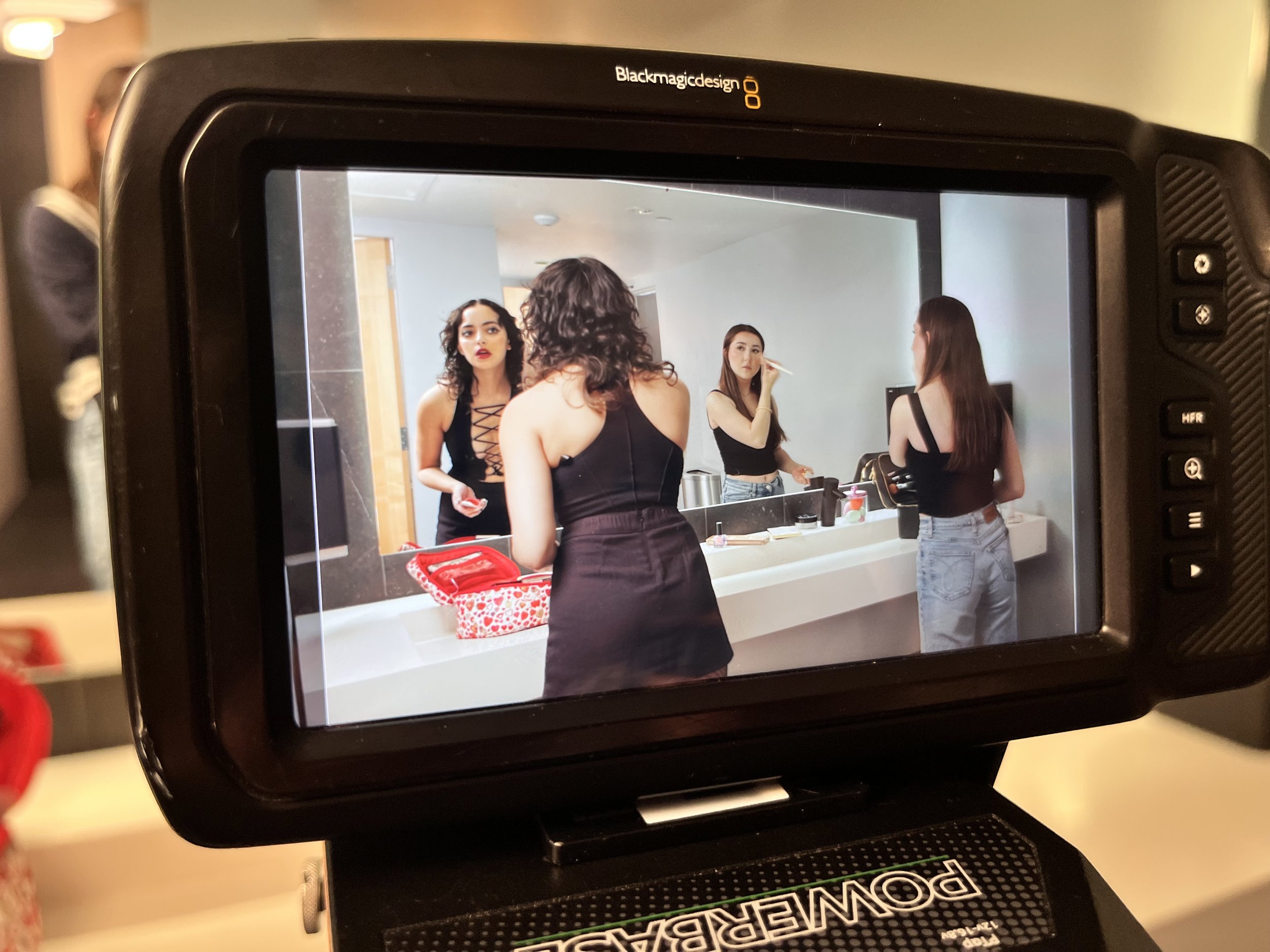 Photograph of a group of four women in black outfits with one woman holding makeup brushes, seen through a camera screen.