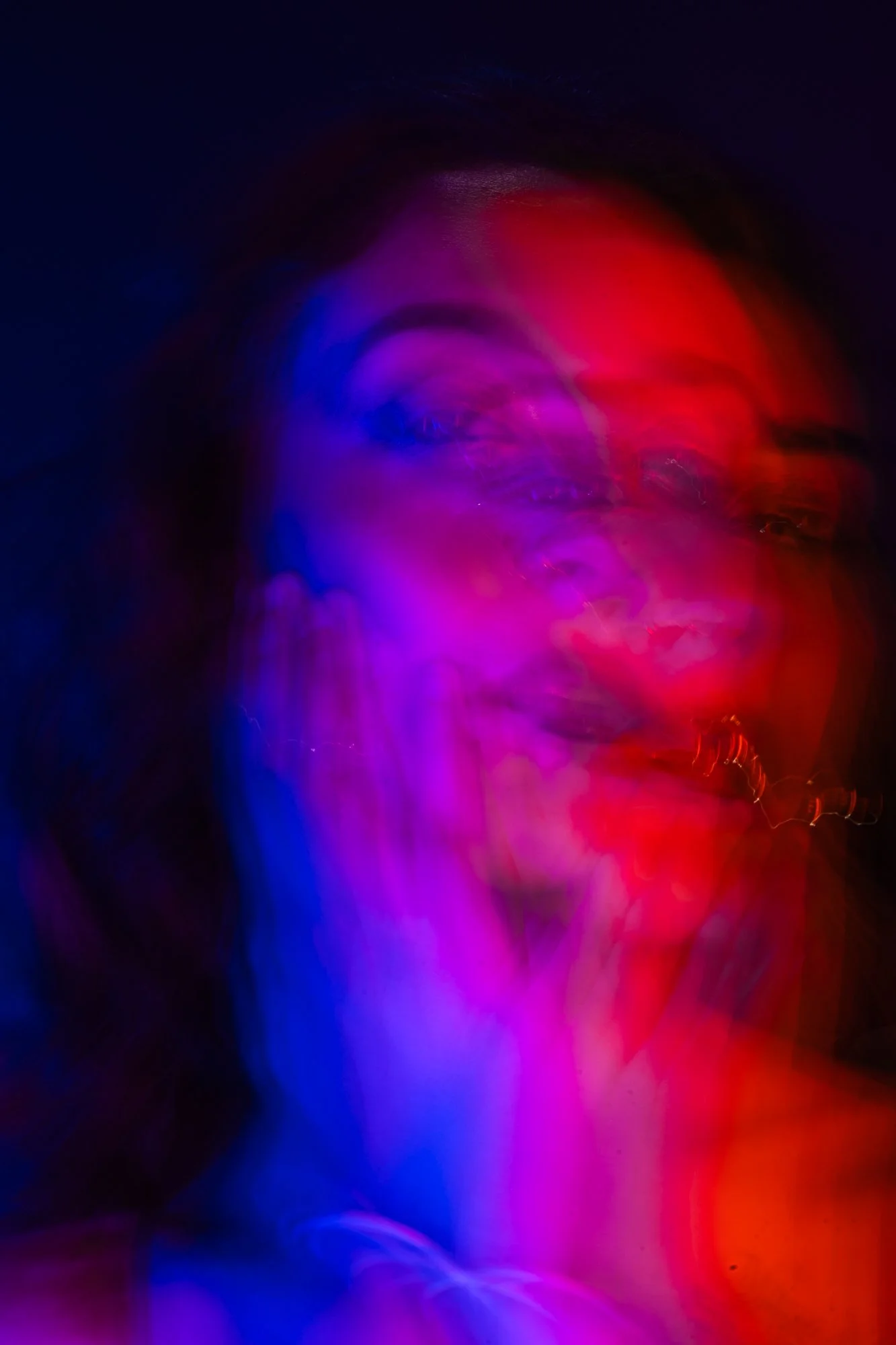 Abstract image of a human face with closed eyes, illuminated by pink, purple, and red neon lights with a blurred effect.
