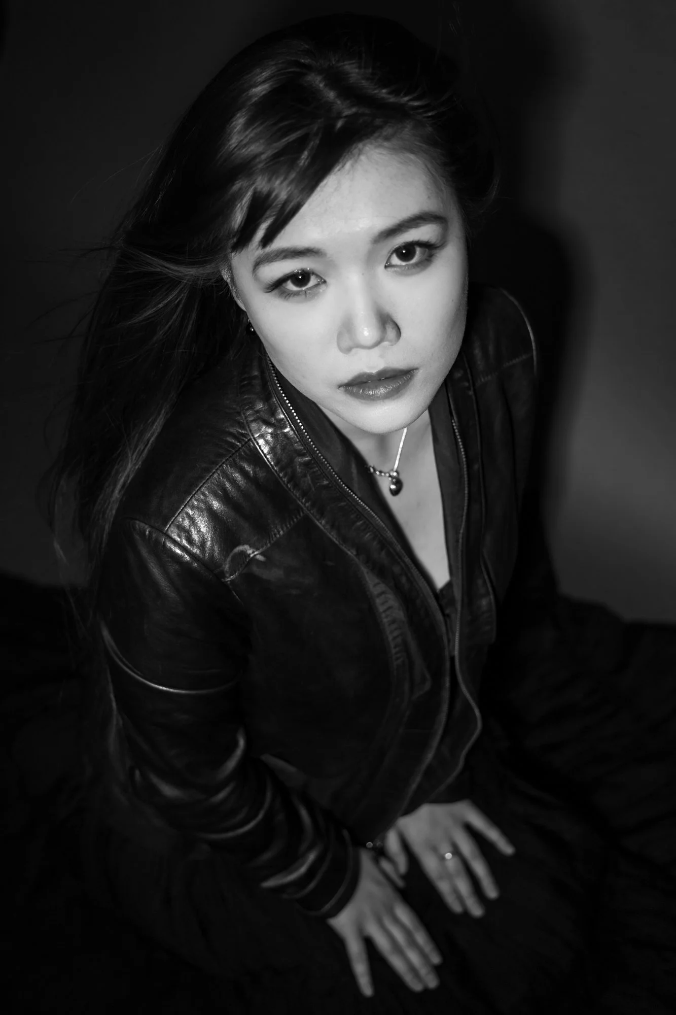 Black and white photo of a woman with long hair, wearing a leather jacket, looking up at the camera.