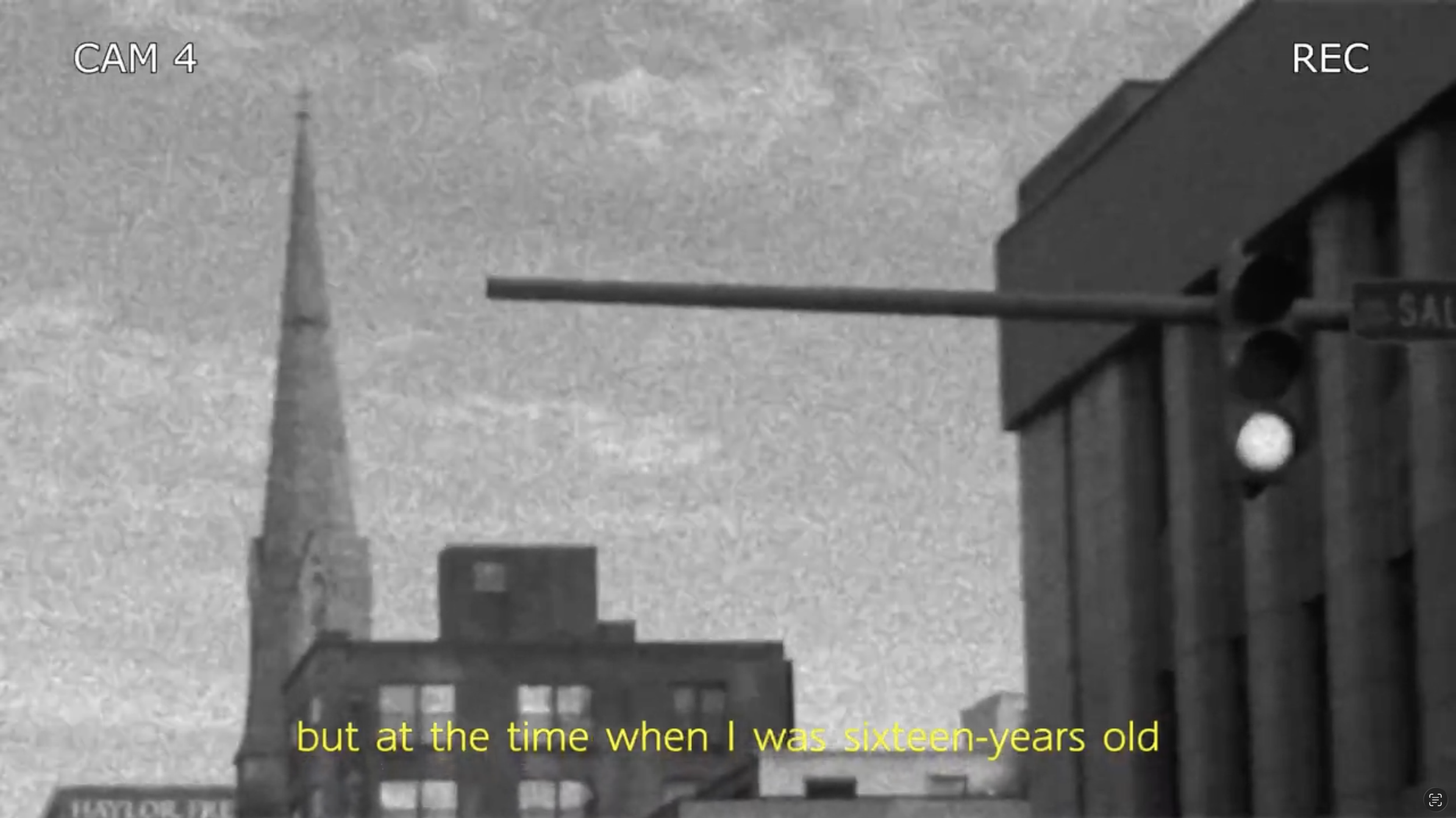 Black and white footage of San Francisco cityscape with the Transamerica Pyramid in the distance. A street scene includes a sign for a hardware store and a person walking on the sidewalk. The image appears on a security or surveillance camera feed, labeled 'CAM 4' and 'REC'. There are yellow subtitles at the bottom that say, 'but at the time when I was sixteen-years old'.