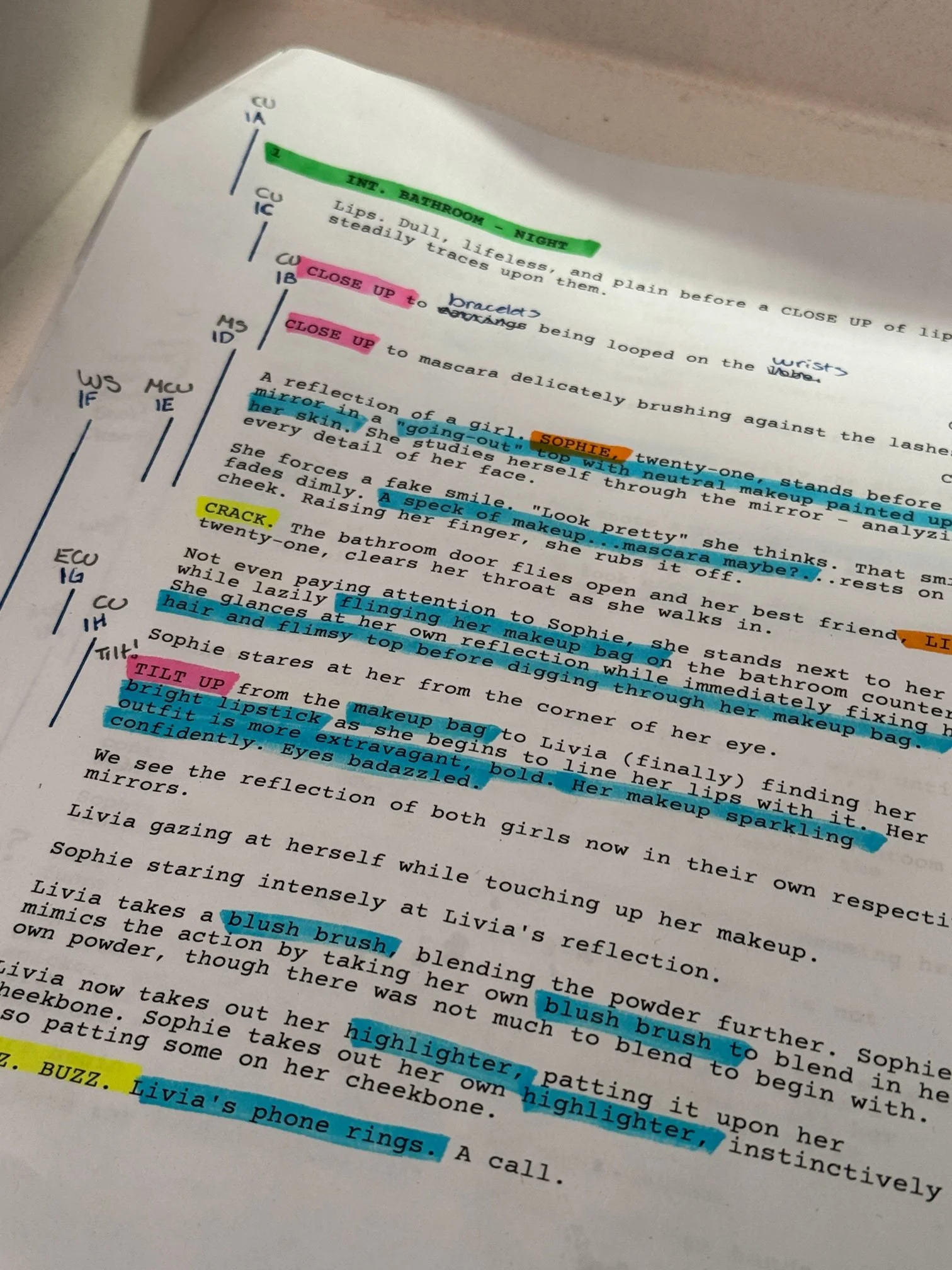 Close-up of a printed page with handwritten and highlighted notes. The notes include colored text highlights in pink, blue, orange, and yellow, with annotations about makeup and facial expressions, along with handwritten comments.