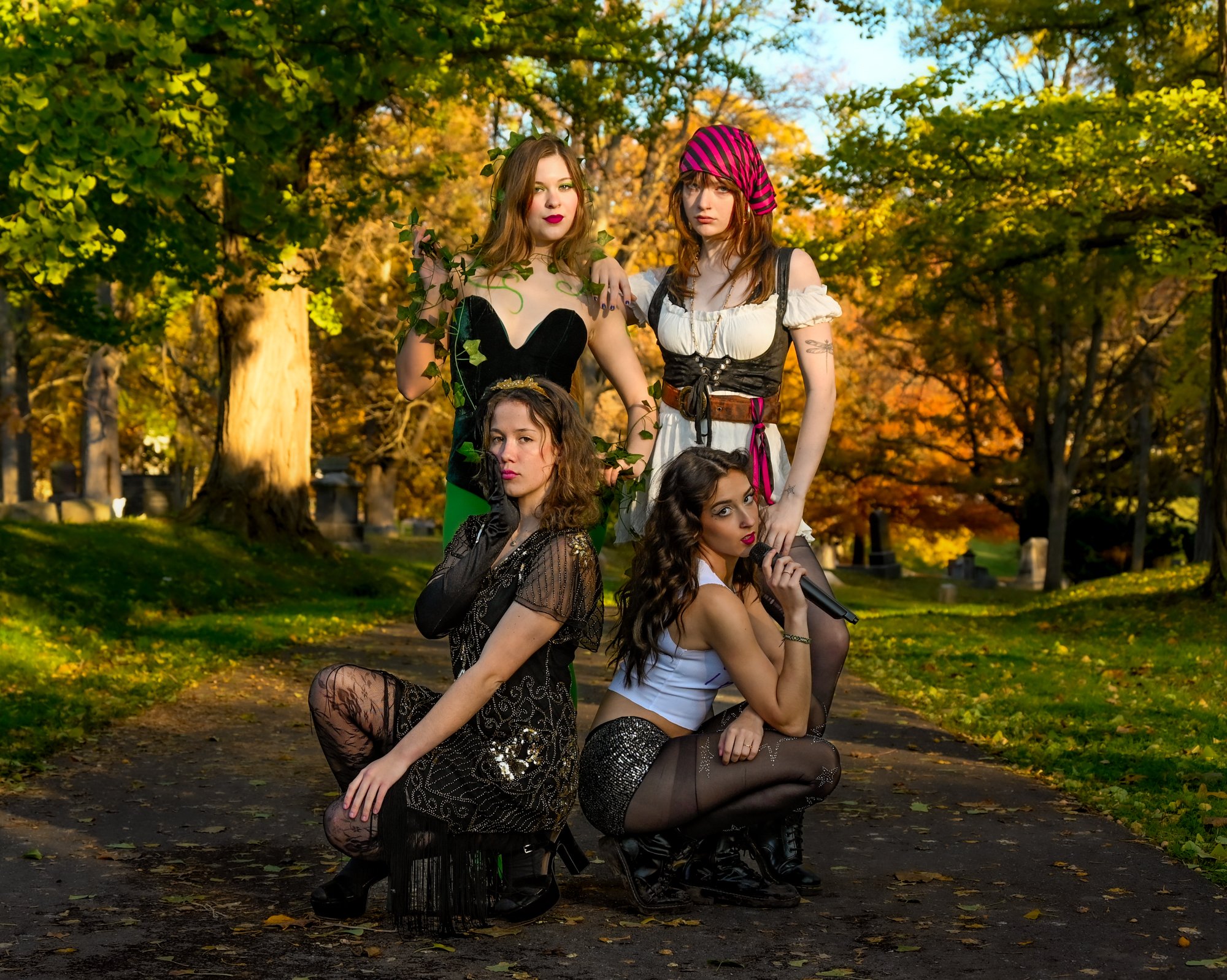 Group of five young women dressed in Halloween costumes posing outdoors in fall foliage.