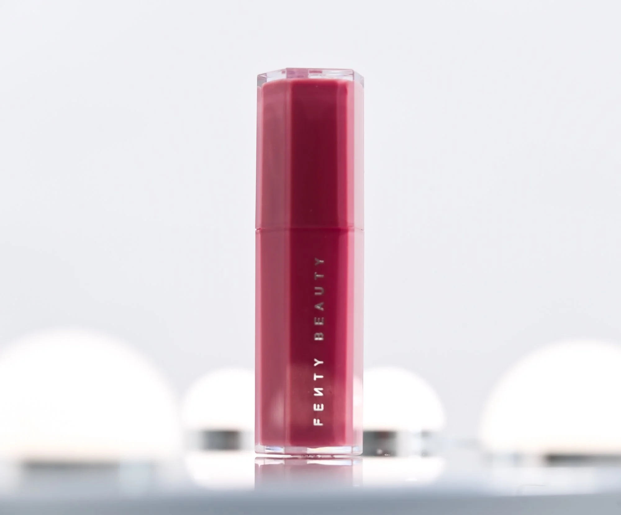 A pink lipstick tube with white text standing upright on a reflective surface, with a white background.