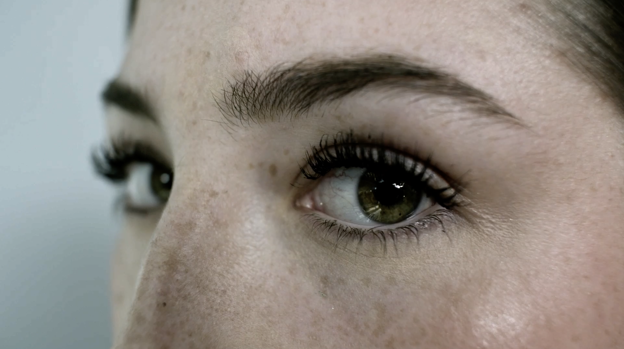 Close-up of a woman's face focusing on her eye, with detailed view of eyelashes, eyebrow, and skin texture.