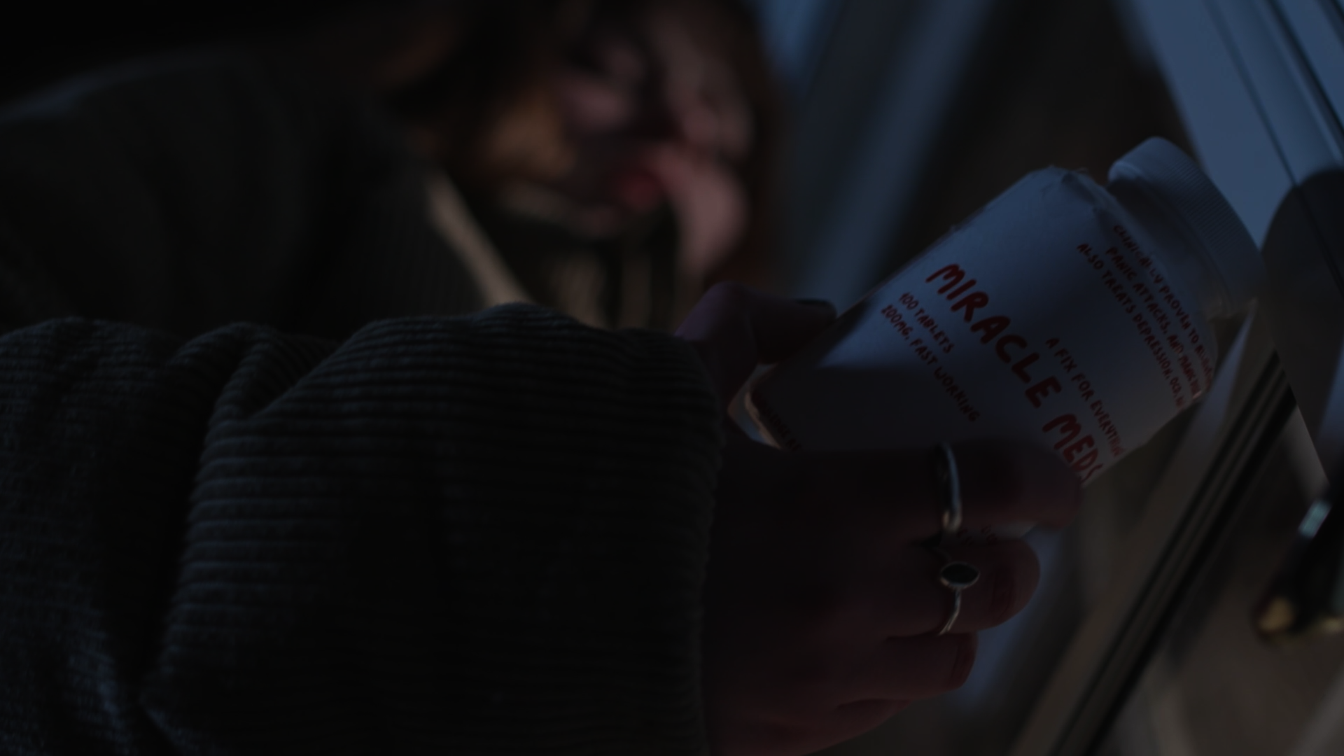 Person holding a bottle labeled 'Miracle Cure' while looking through a window.