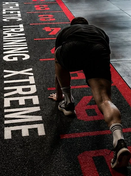 Ein männlicher Athlet im Startblock in einer Turnhalle, bereit für einen Sprint.