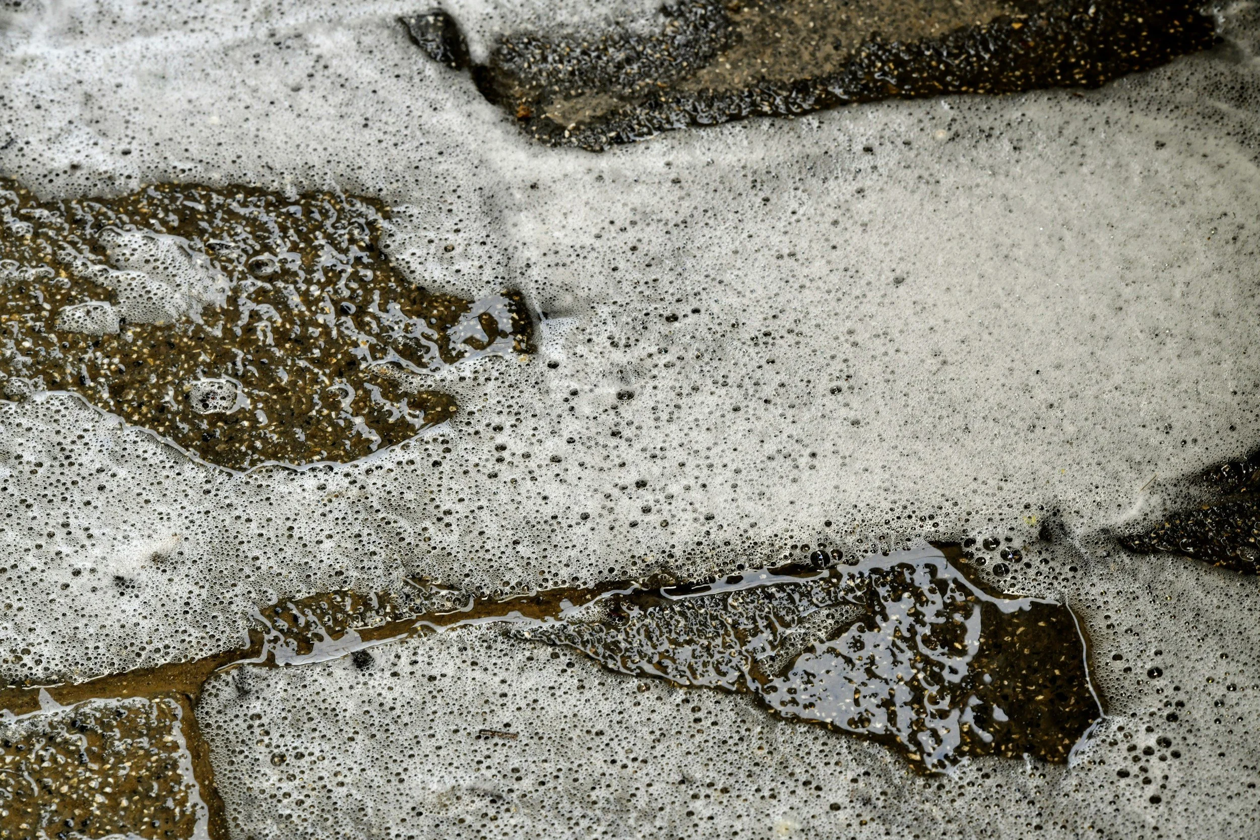 Close-up of beach sand with foamy ocean waves washing over it.