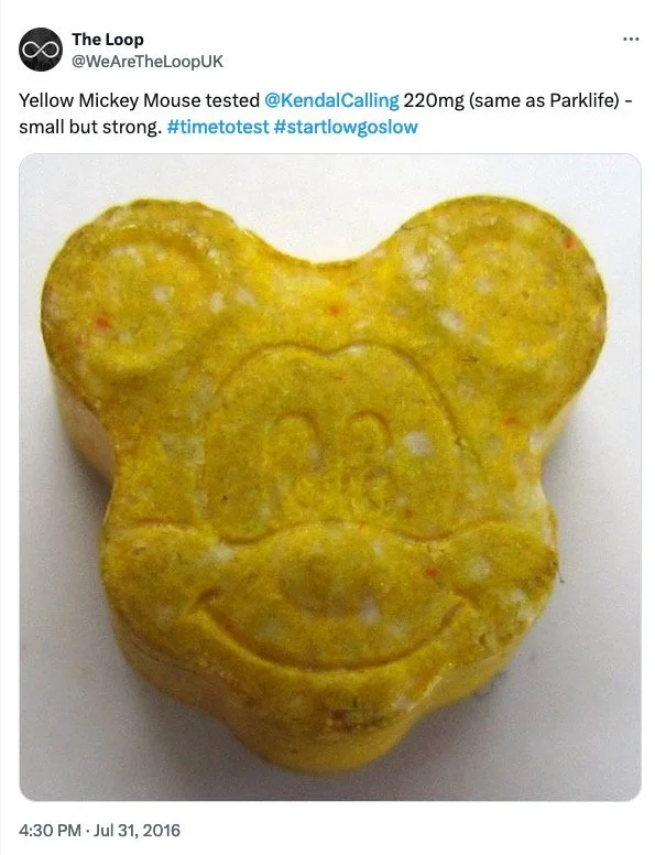 A yellow Mickey Mouse-shaped pill or supplement with a smiley face and Mickey Mouse ears embossed on the surface.