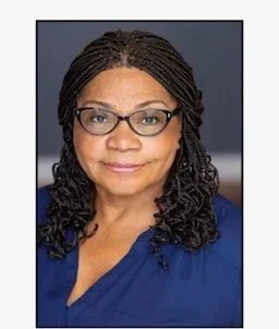 A woman with braids and glasses, wearing a blue top, smiling softly for the portrait.