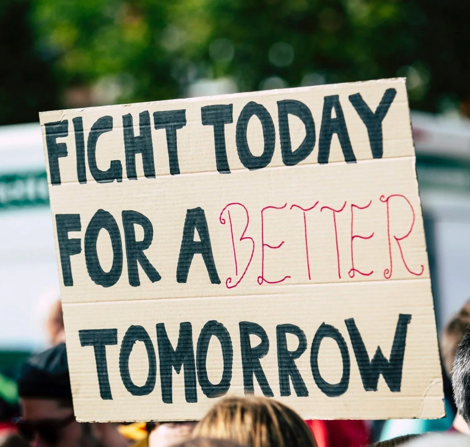 Handwritten sign reading 'Fight Today for a Better Tomorrow' at a protest or rally, with a blurred crowd in the background.