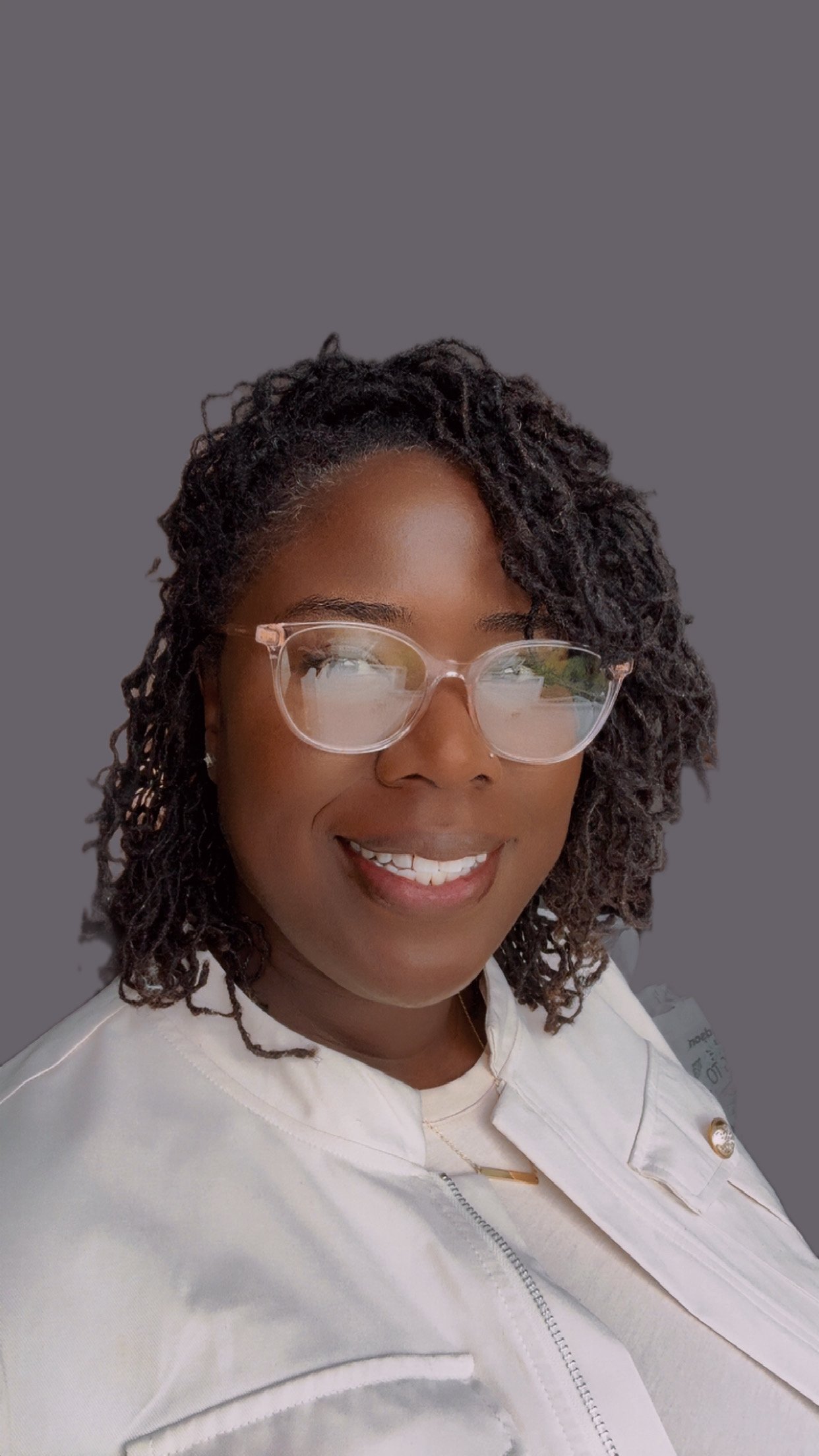 A woman with curly hair, glasses, and a white jacket smiling against a gray background.