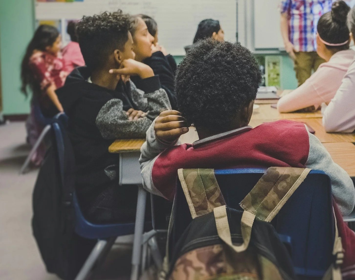 Students sitting at desks in a classroom listening to a teacher or presentation.