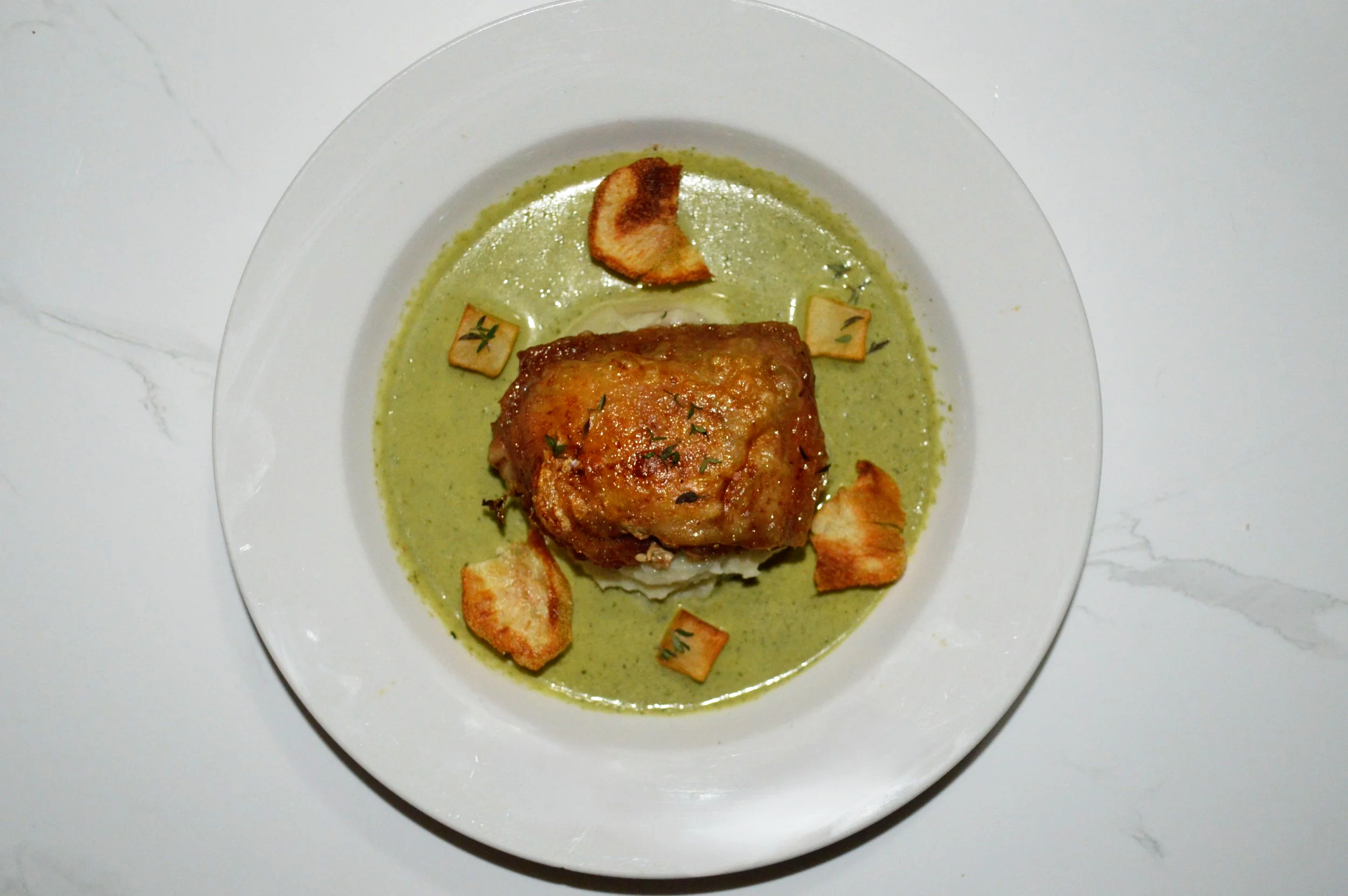 Crispy skin chicken thigh plated on a bed of pea puree, with potato chips