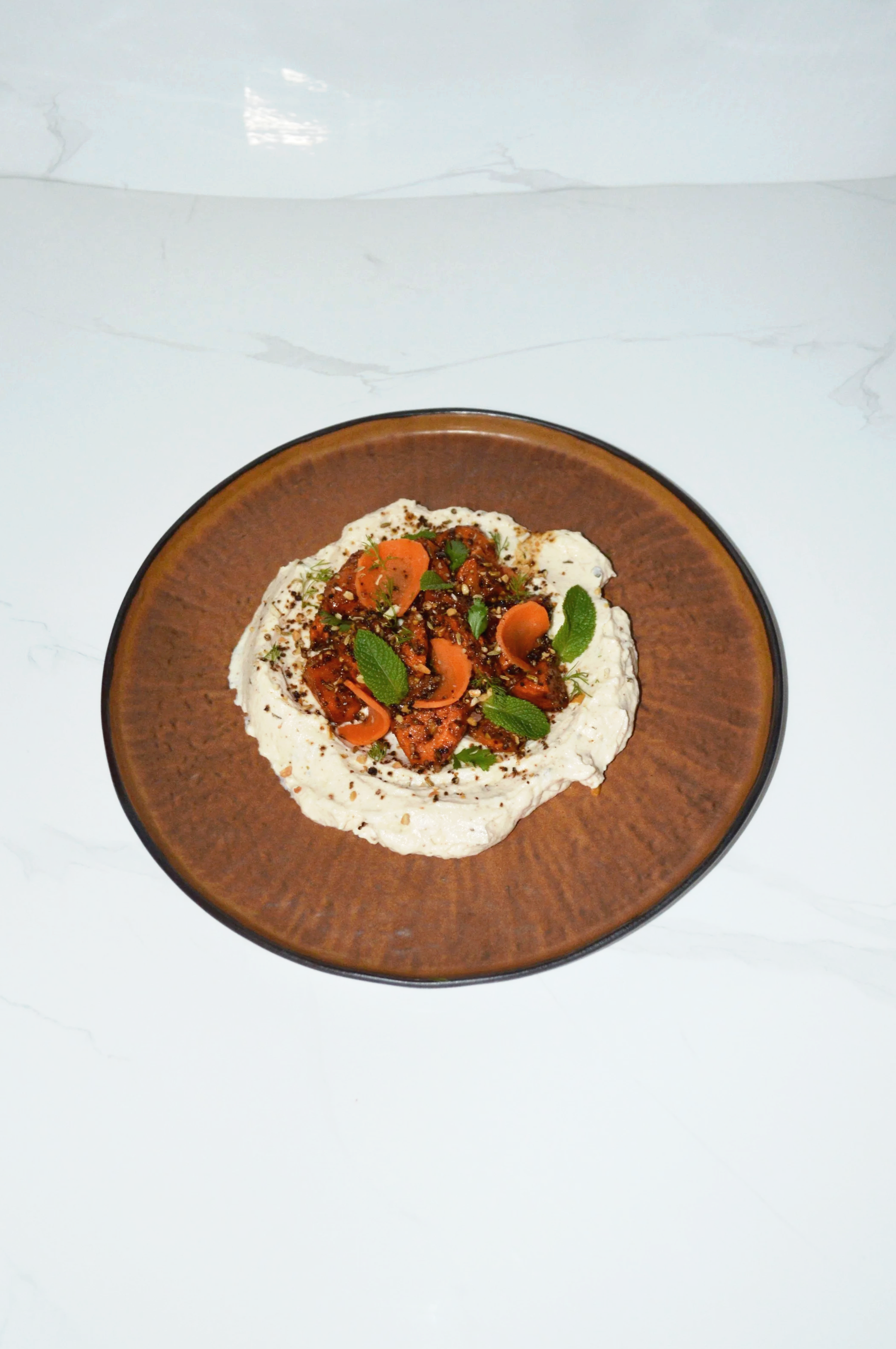 A plate of harissa carrots served on a spiced labneh