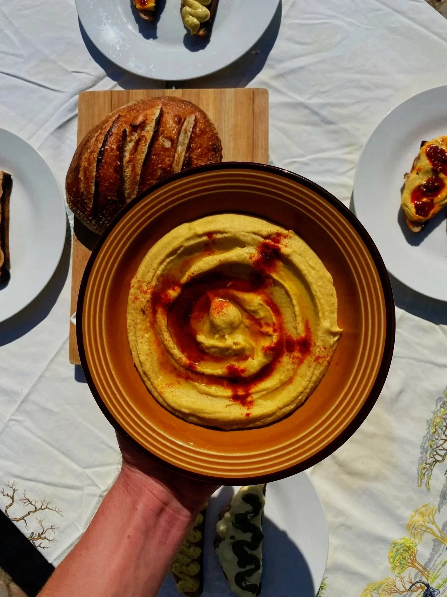 A plate of hummus with a Sourdough loaf in the background