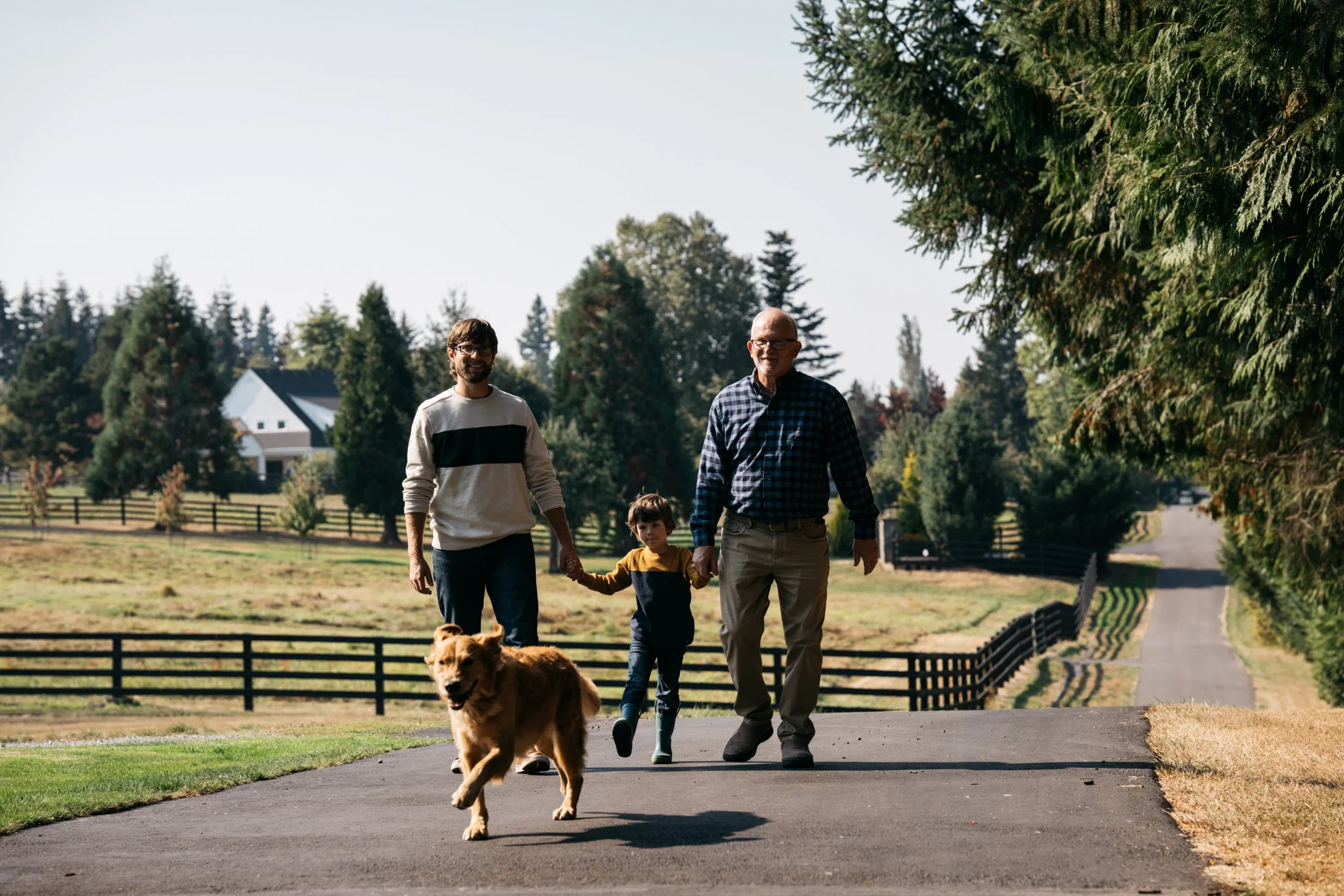 A family walking in a park with a dog on a leash, trees and a house in the background.