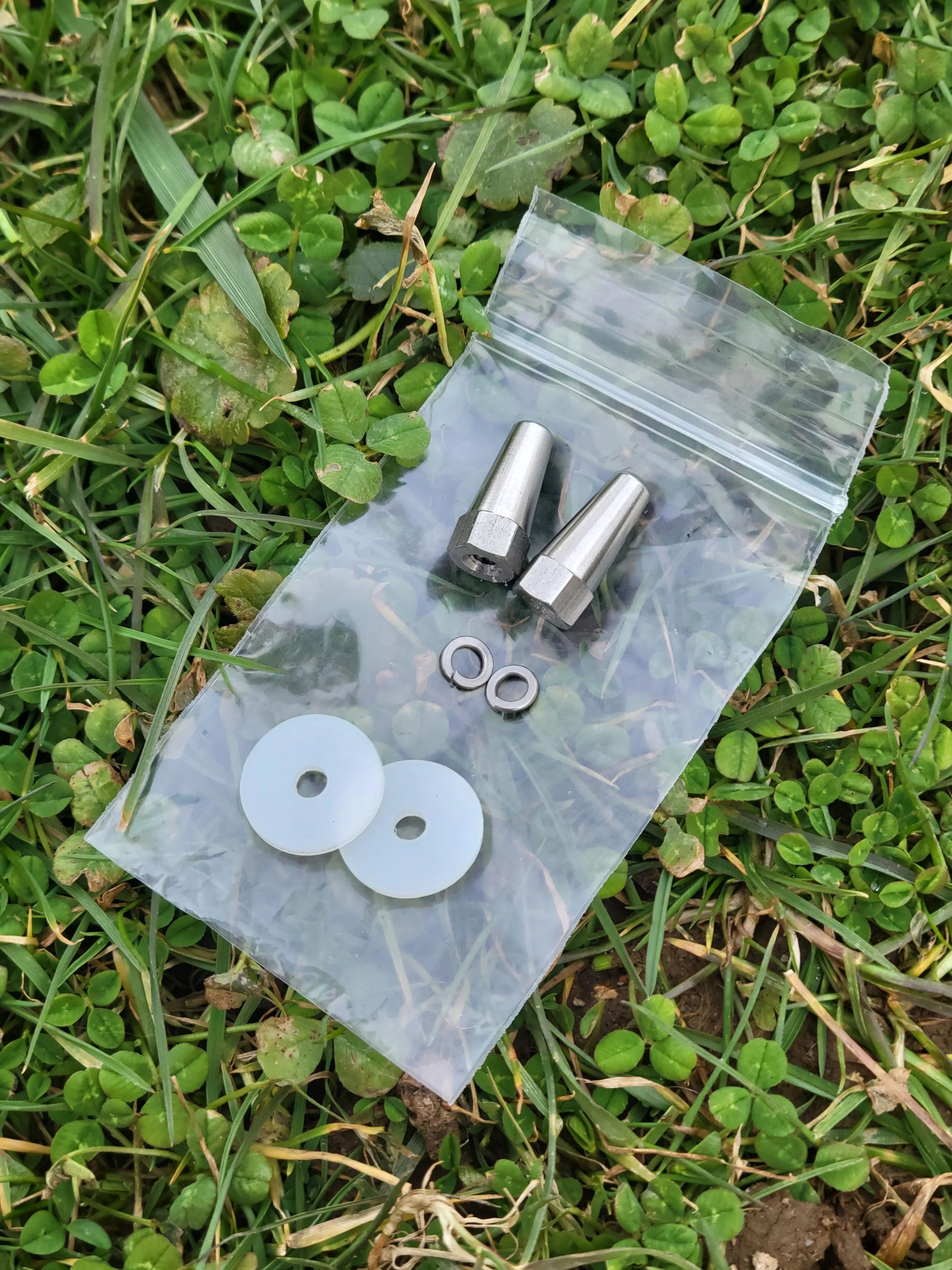 Two metal fittings and washers inside a plastic bag on grass.