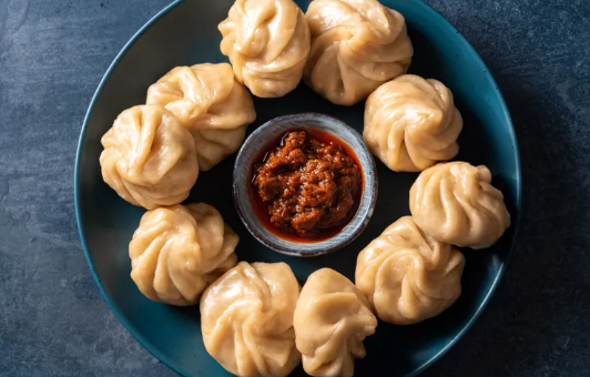 Teigtaschen (Momos) auf einem Teller mit einer scharfen Soße in der Mitte.