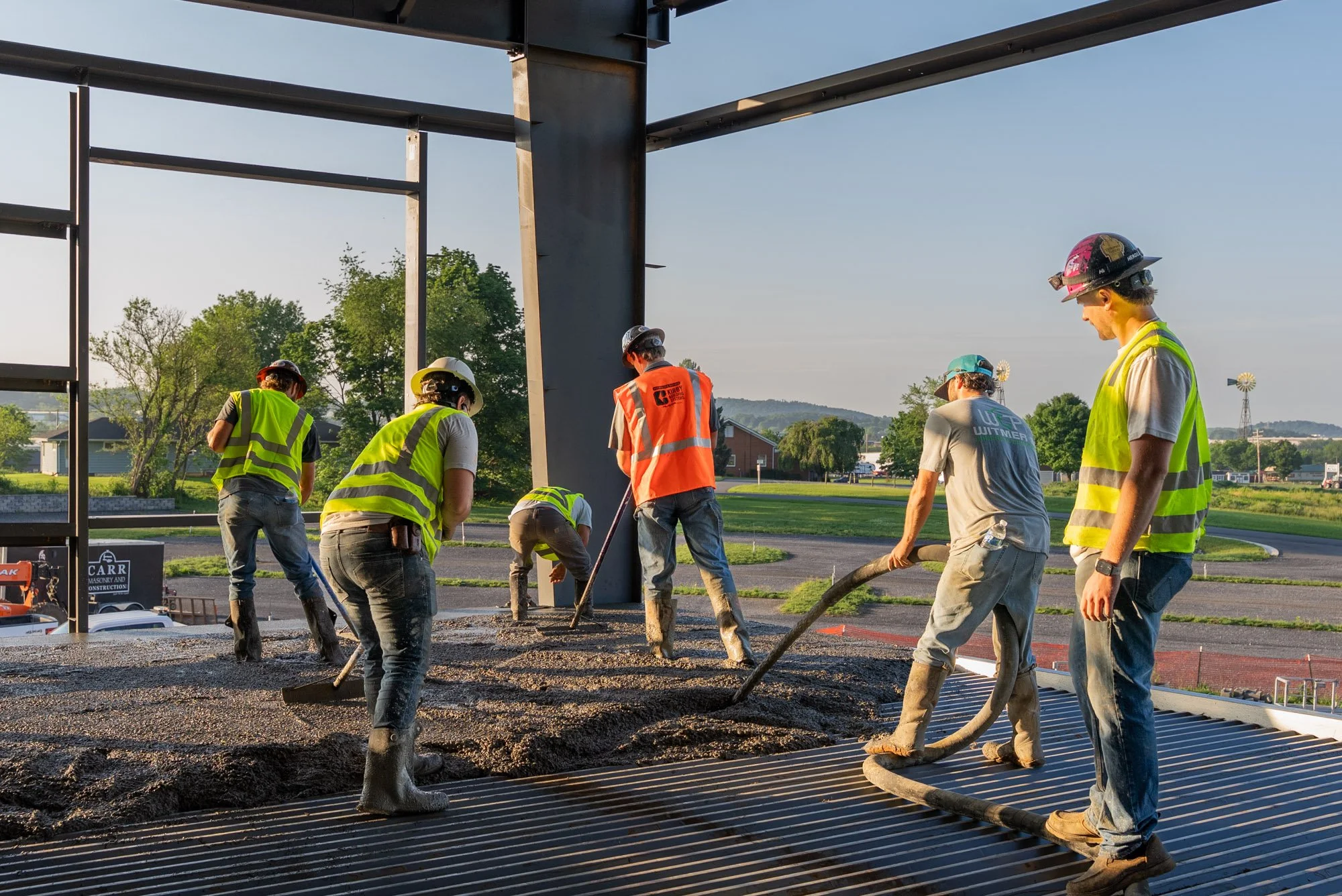 Construction workers wearing safety vests and helmets pouring asphalt on a road during daylight.