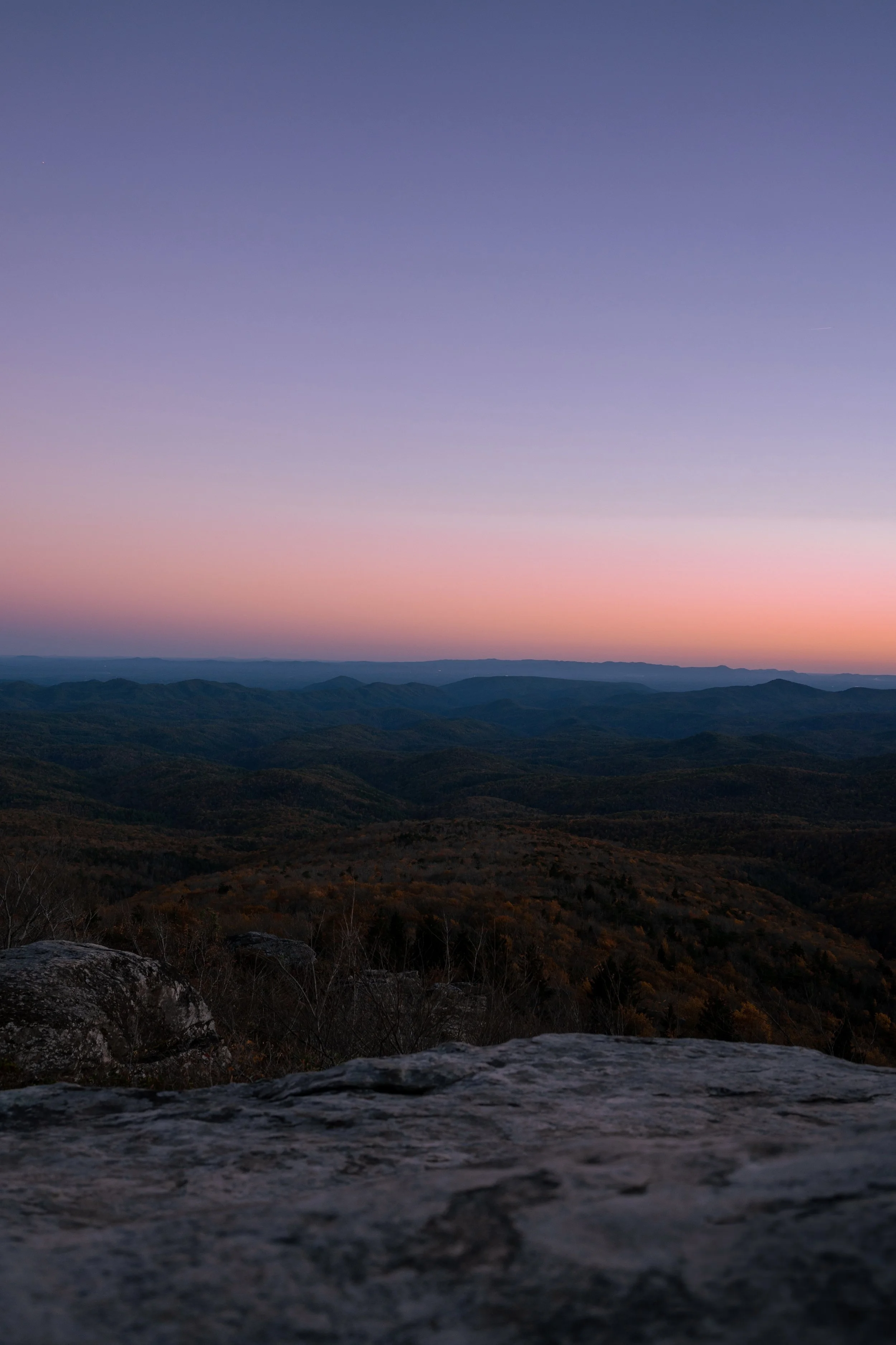 Scenic view of mountains with a pastel-colored sky during sunrise or sunset, with clouds near the horizon.