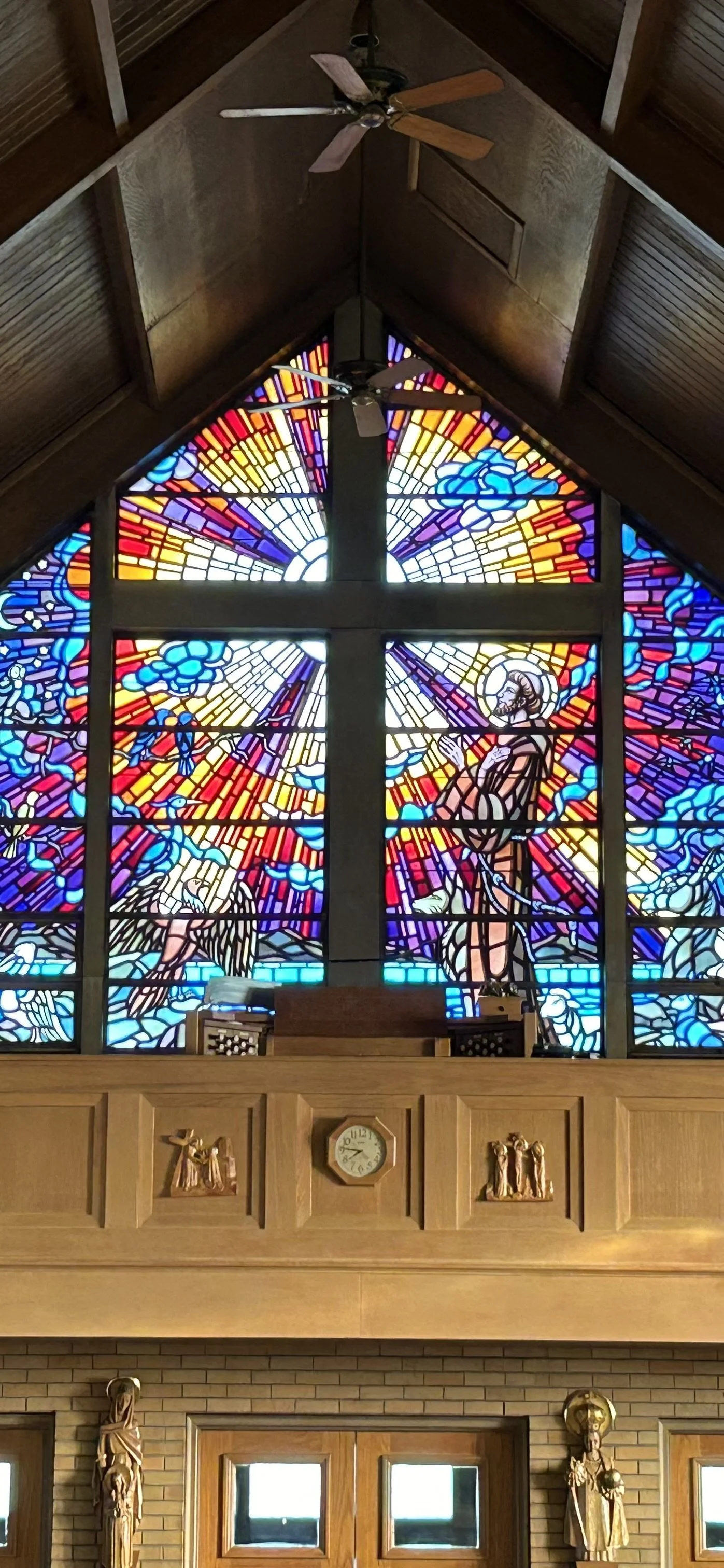 Stained glass window depicting the Resurrection of Jesus Christ with rays of light, clouds, angels, and Jesus standing with a halo in a church interior.