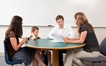 teacher, parents, and student talking together around a table and looking at papers
