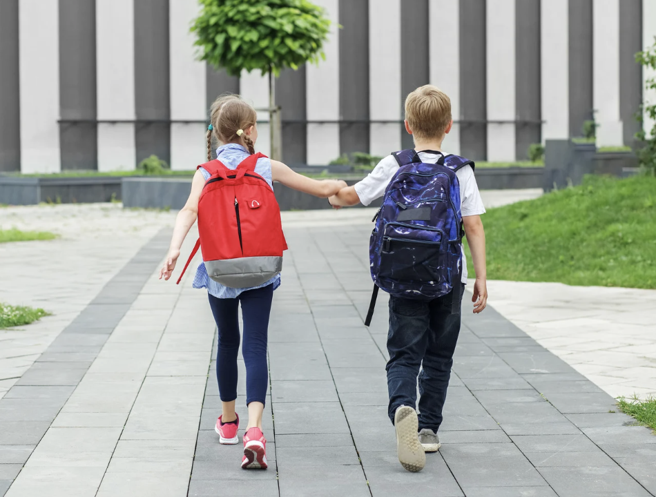 two children with back packs holding hands and walking into school