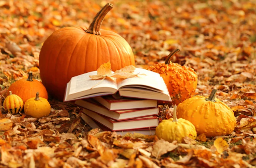 stack of books surrounded by fall leaves and pumpkins