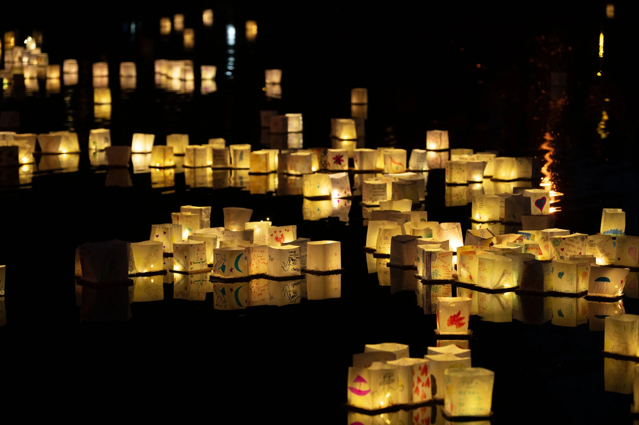 Many illuminated paper lanterns floating on a body of water at night, with some lanterns reflecting in the water.