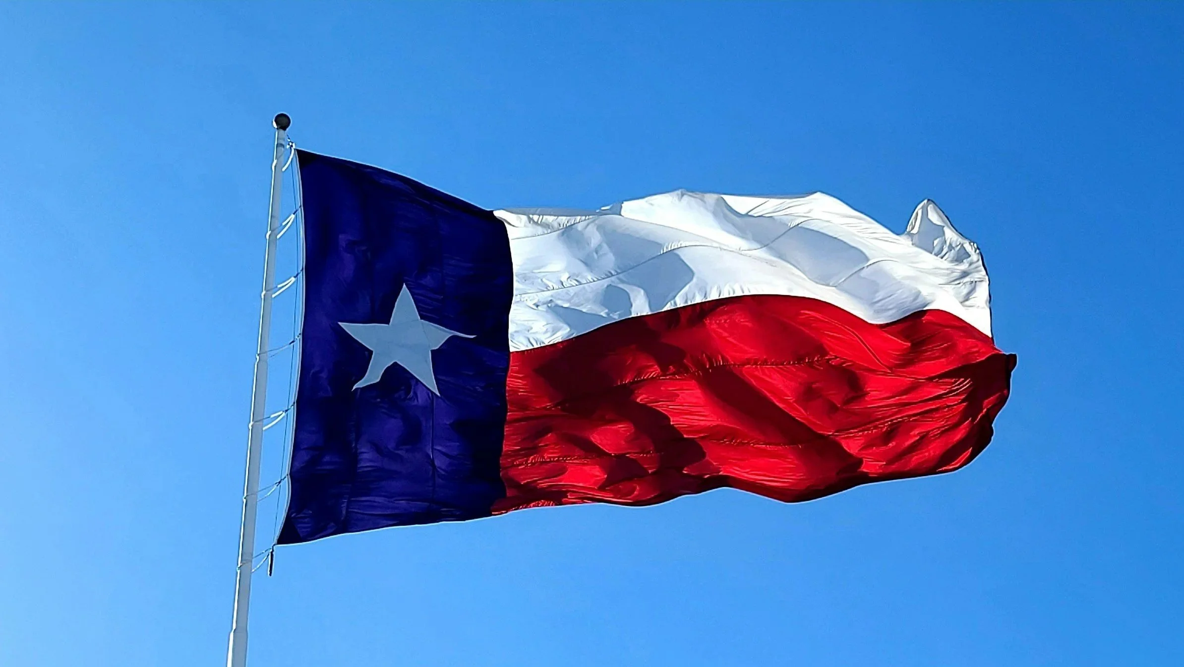 The Texas state flag waving in the wind against a clear blue sky.