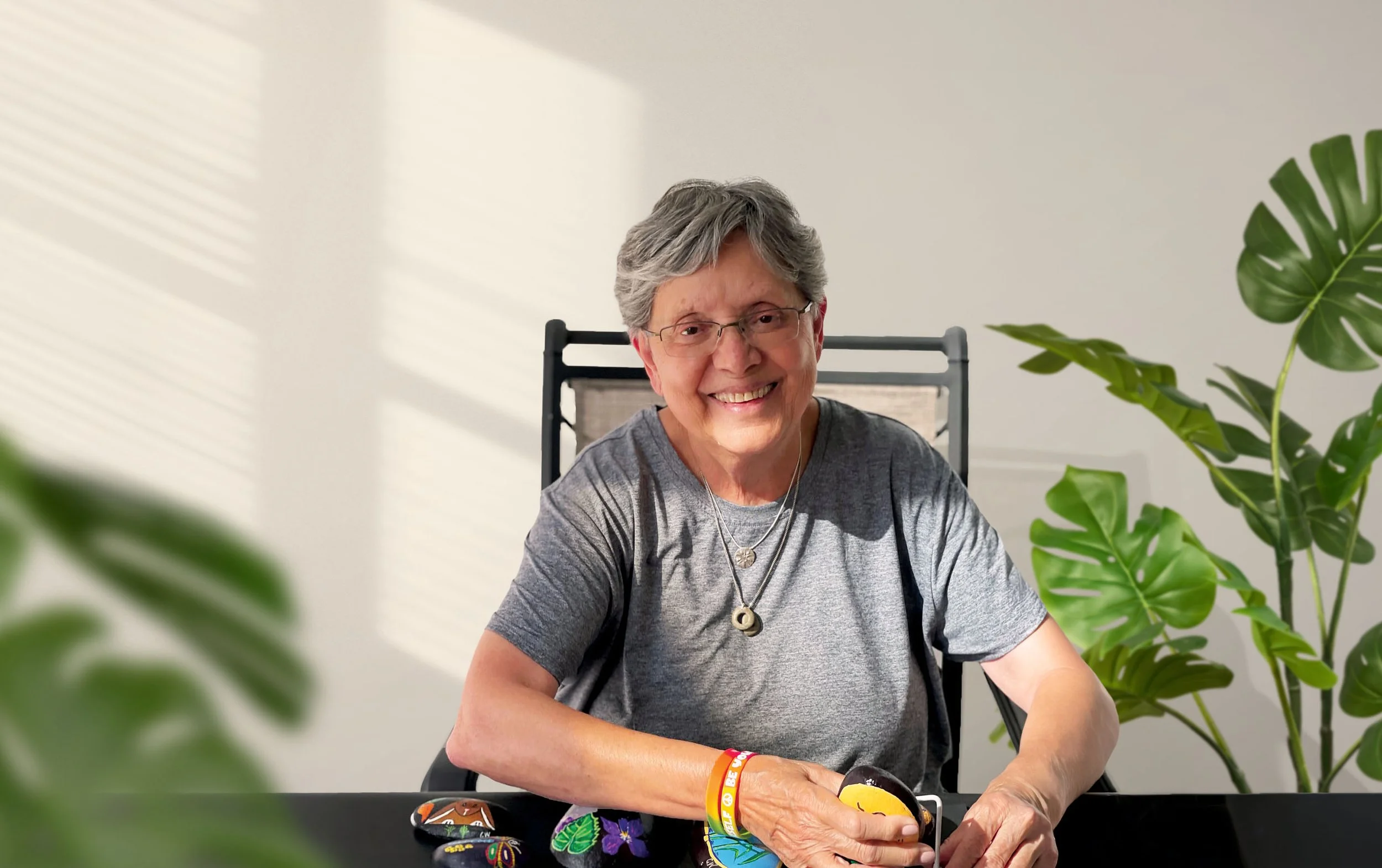 Cynthia Winter smiling at her worktable, holding one of a group of small painted stones.