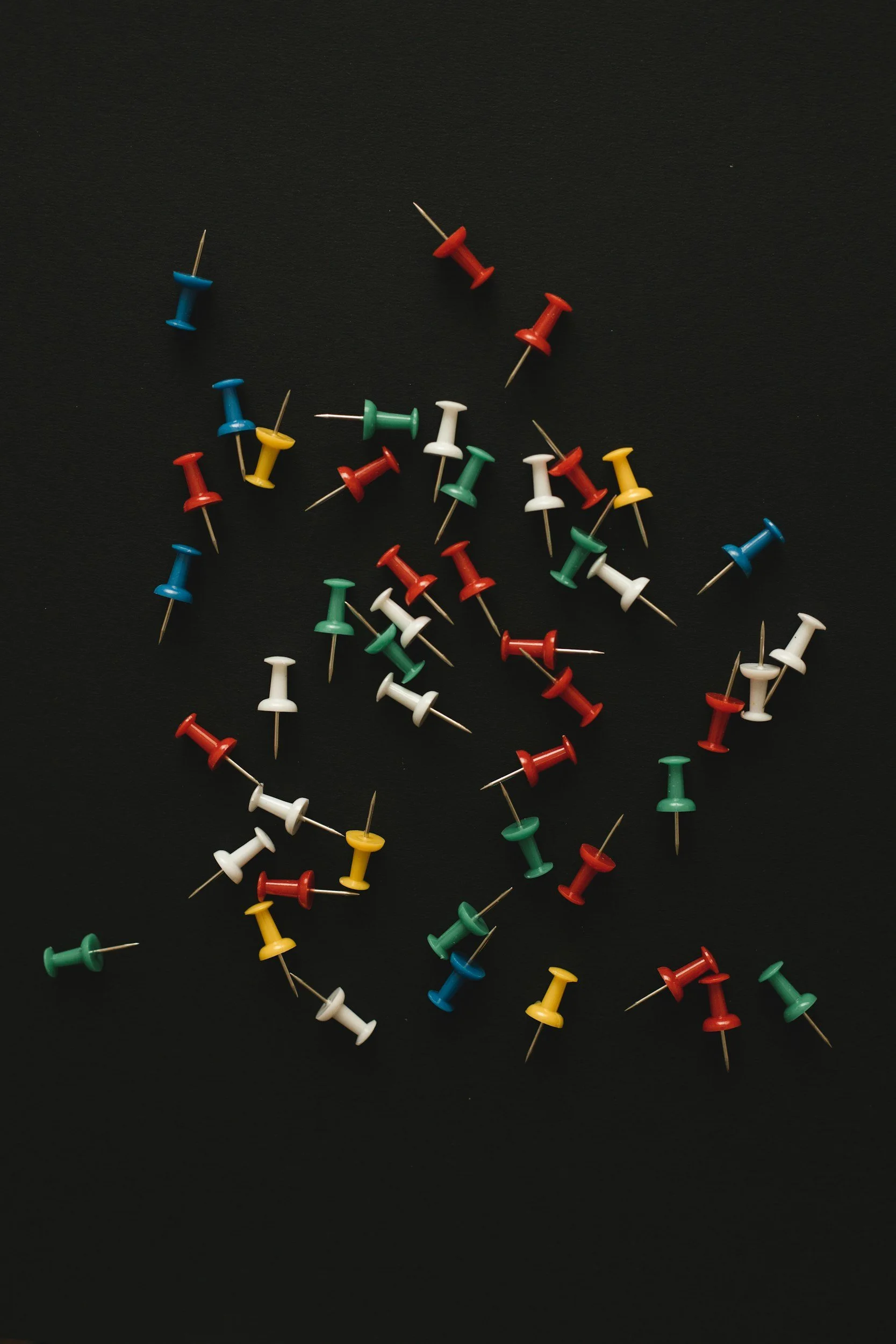 Colorful push pins scattered on a black surface.