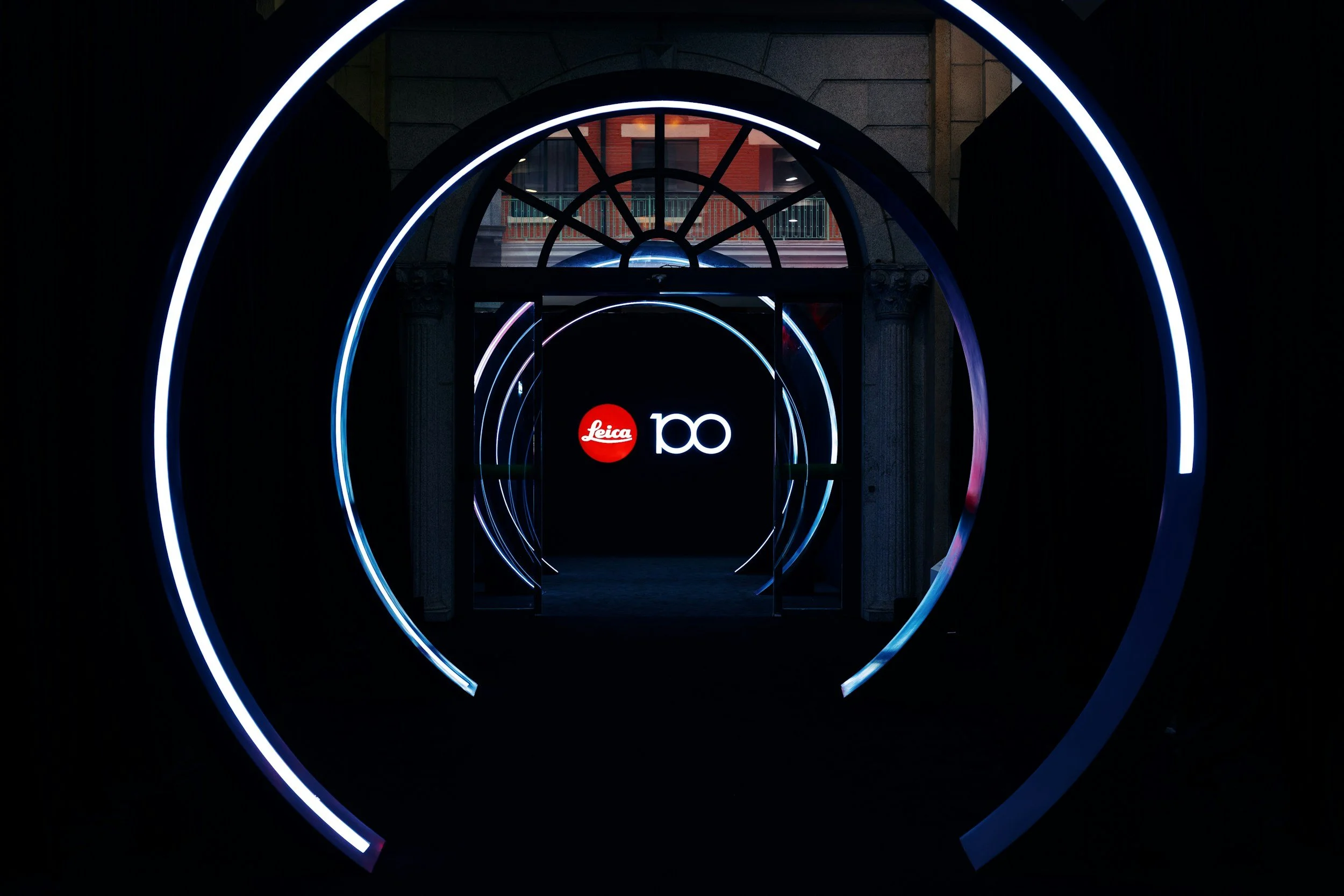 Illuminated circular tunnel with neon lights and a sign that reads 'Leica 100' at the end.
