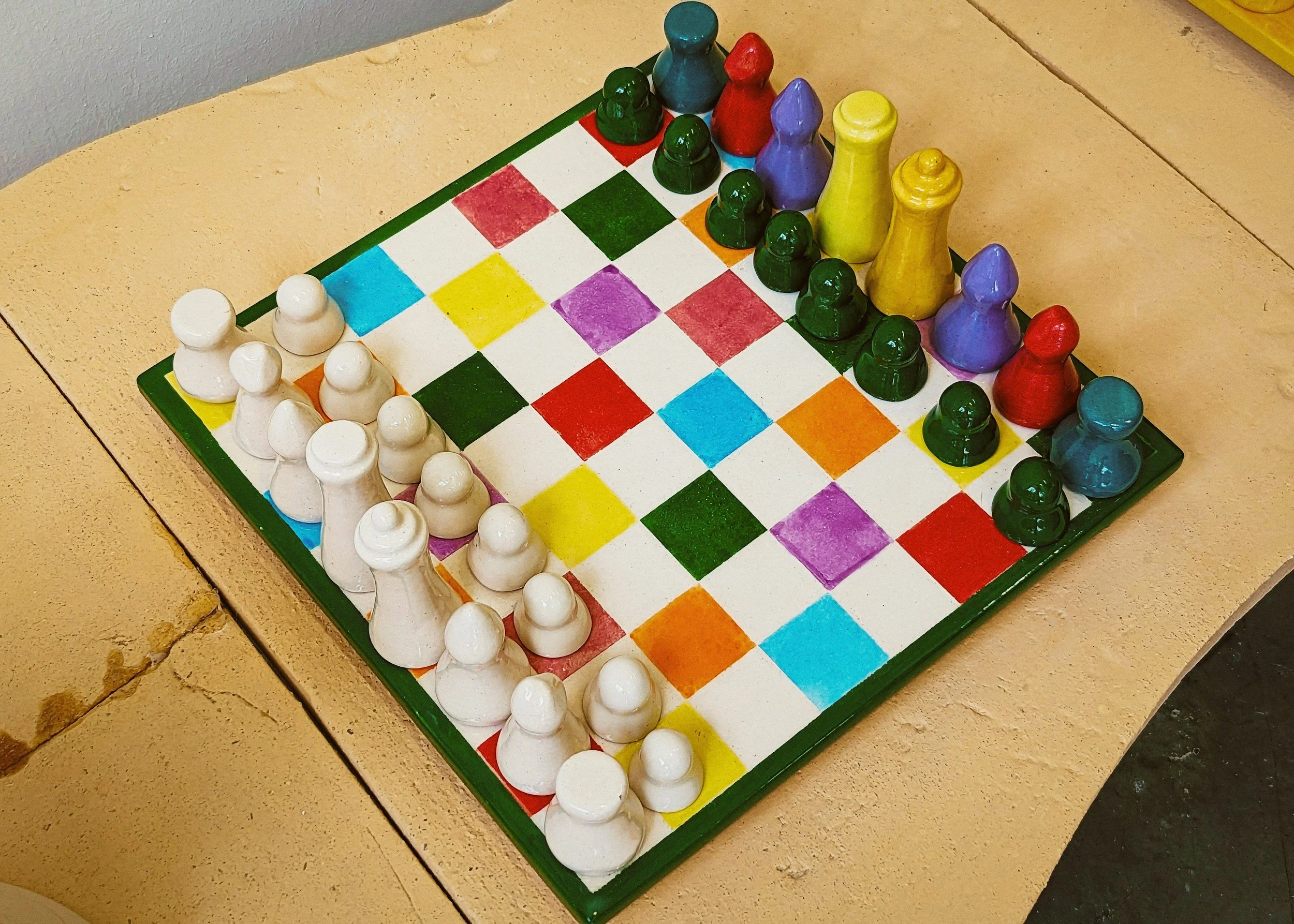 Colorful chessboard with painted game pieces on a light wooden surface.