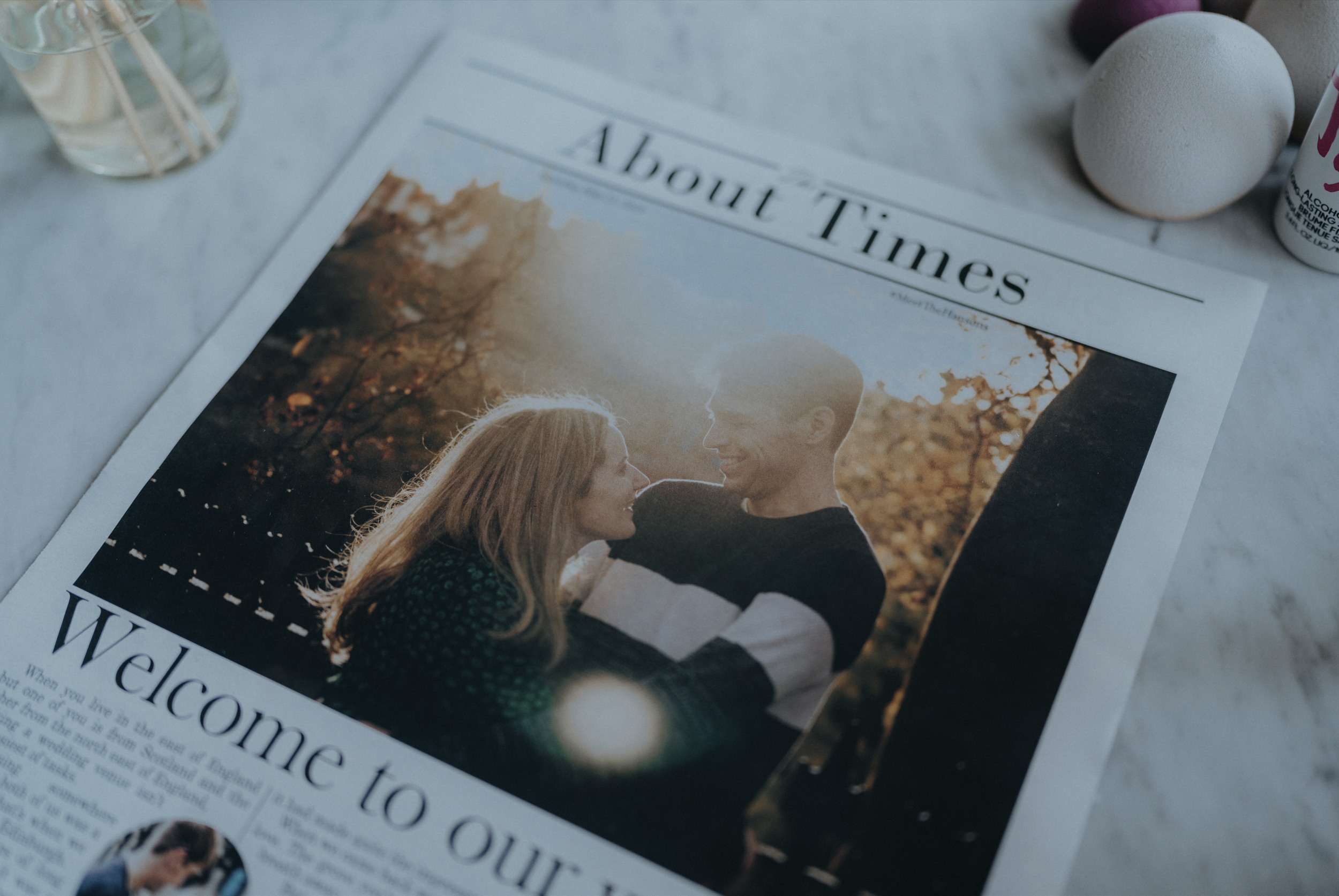 A magazine or newspaper page featuring a romantic photo of a couple with a sunset background, surrounded by various objects including a white foam ball, a purple sphere, and a small white bottle, possibly lotion or sanitizer, on a light-colored surface.