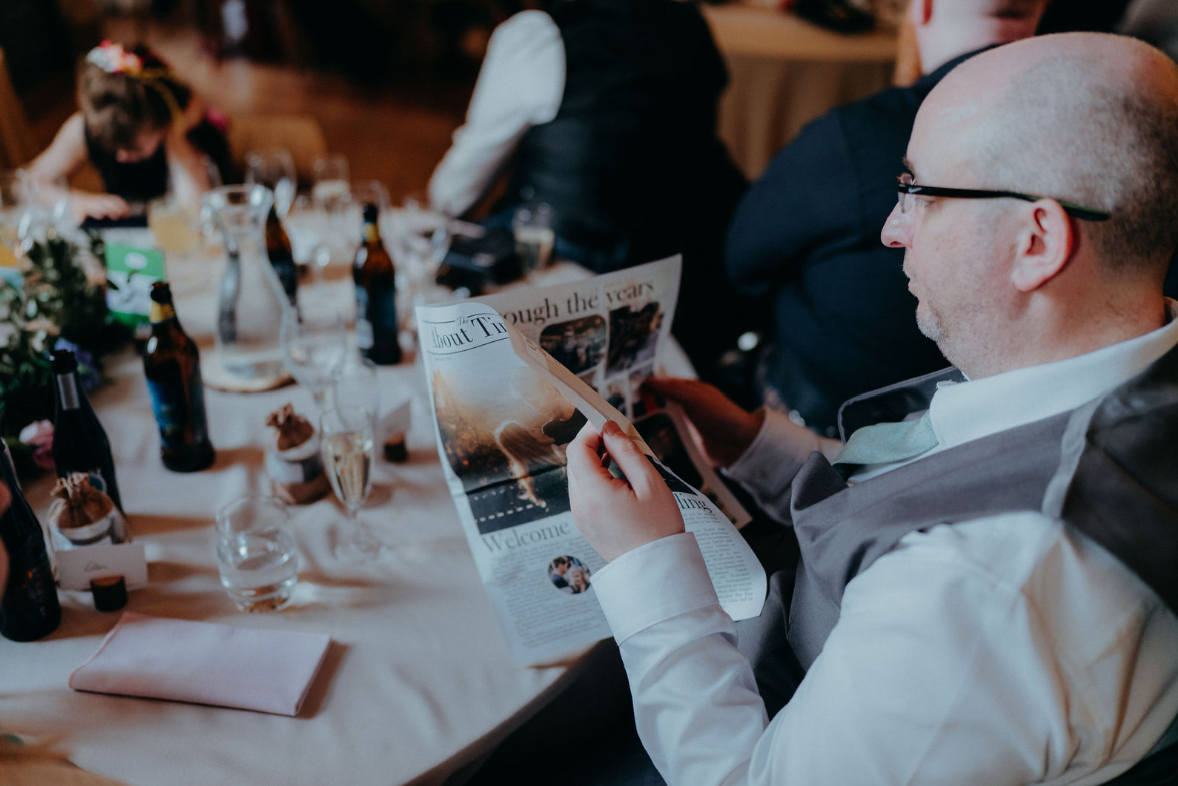 Male wedding guest reading a personalised wedding newspaper at the reception.