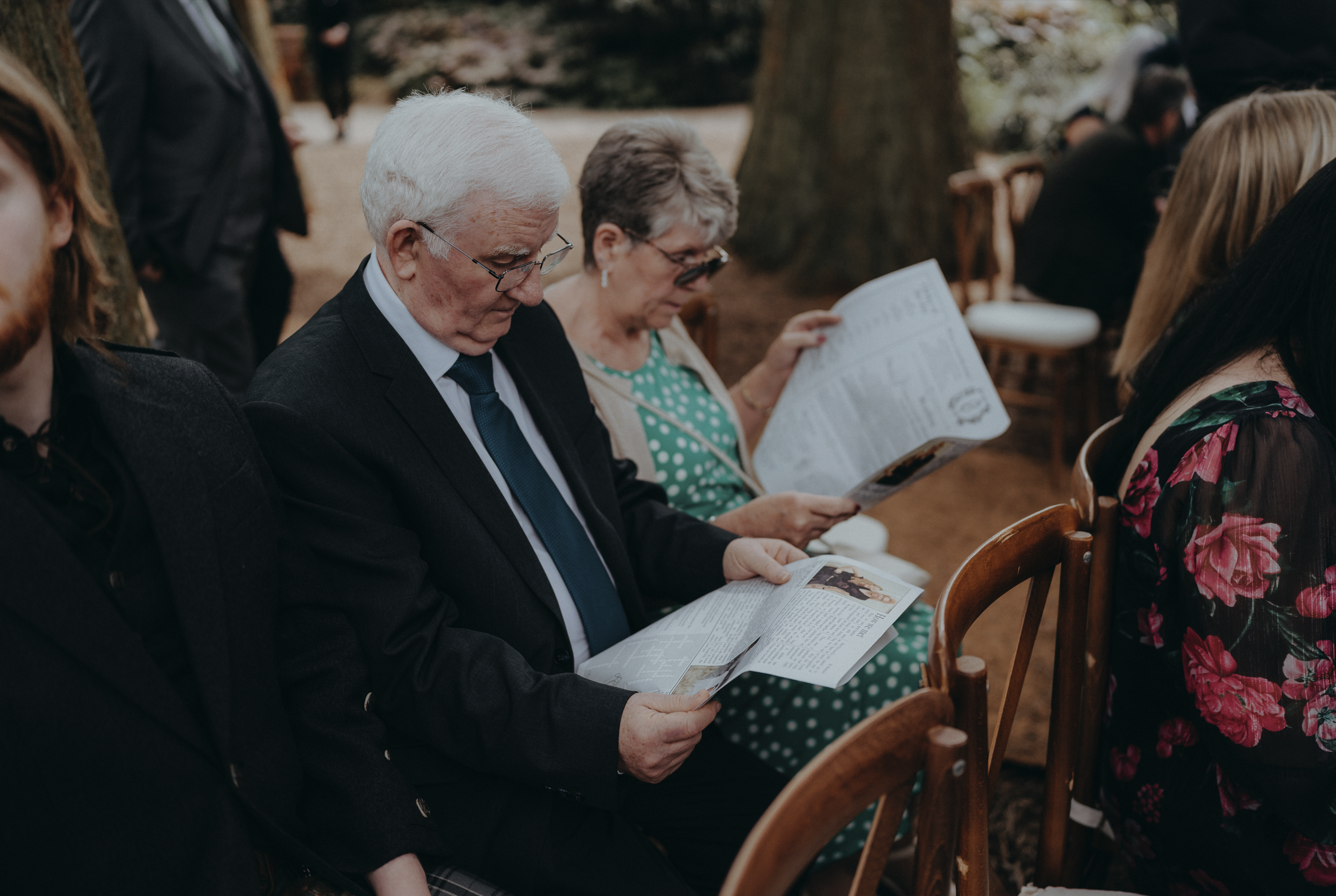 Wedding guests reading personalised newspapers during an outdoor wedding ceremony.