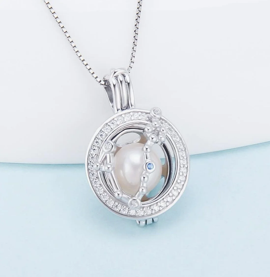 Silver pendant necklace featuring a pearl surrounded by a circular design with small diamonds and decorative elements on a silver chain.