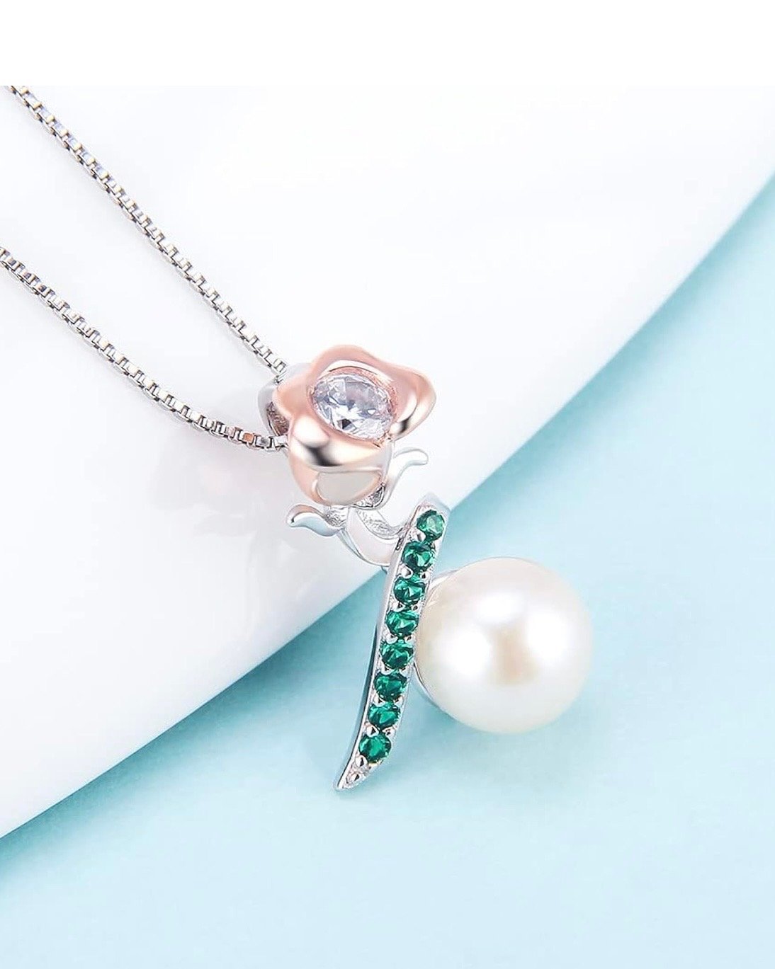 Jewelry necklace with a flower-shaped pendant, green gemstones, a pearl, and a white background.
