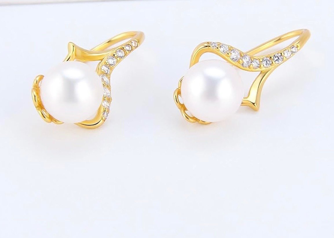 Gold earrings with pearl centers and embedded small diamonds, positioned against a white background.