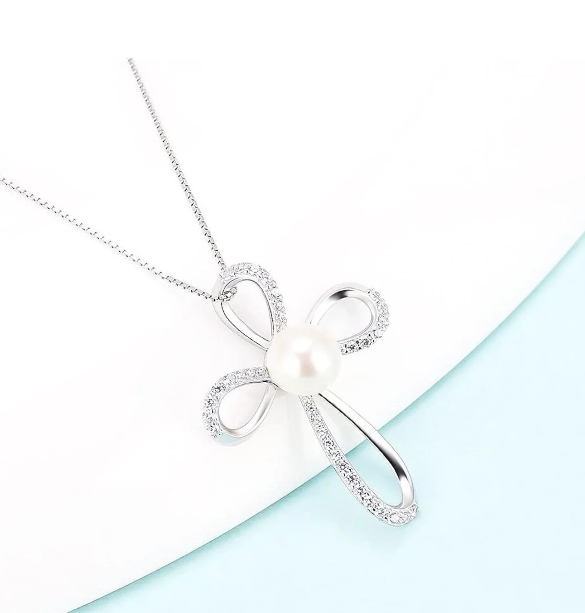 Silver necklace with a butterfly-shaped pendant adorned with small gemstones and a central pearl, on a white and light blue background.