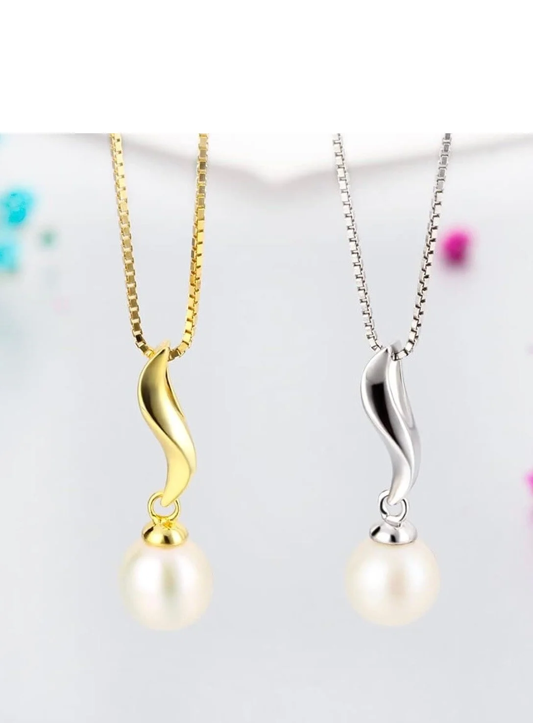 Two necklaces with wave-shaped pendants, one gold and one silver, each with a pearl at the bottom, hanging against a white background.