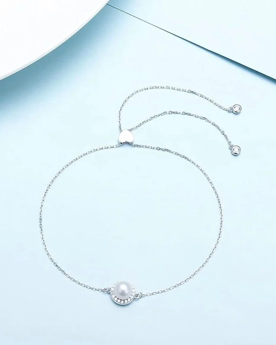 Set of silver jewelry including a necklace with a pearl pendant, a bracelet, and a pair of drop earrings, displayed on a light blue surface.