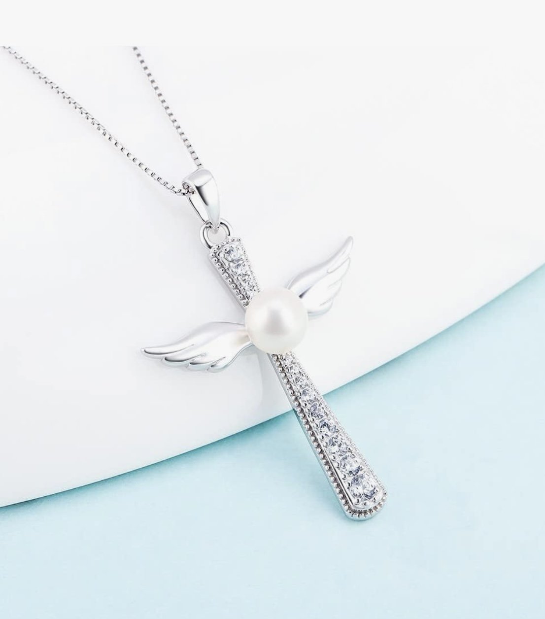 Silver necklace with angel pendant featuring a pearl and crystals, against a white and light blue background.
