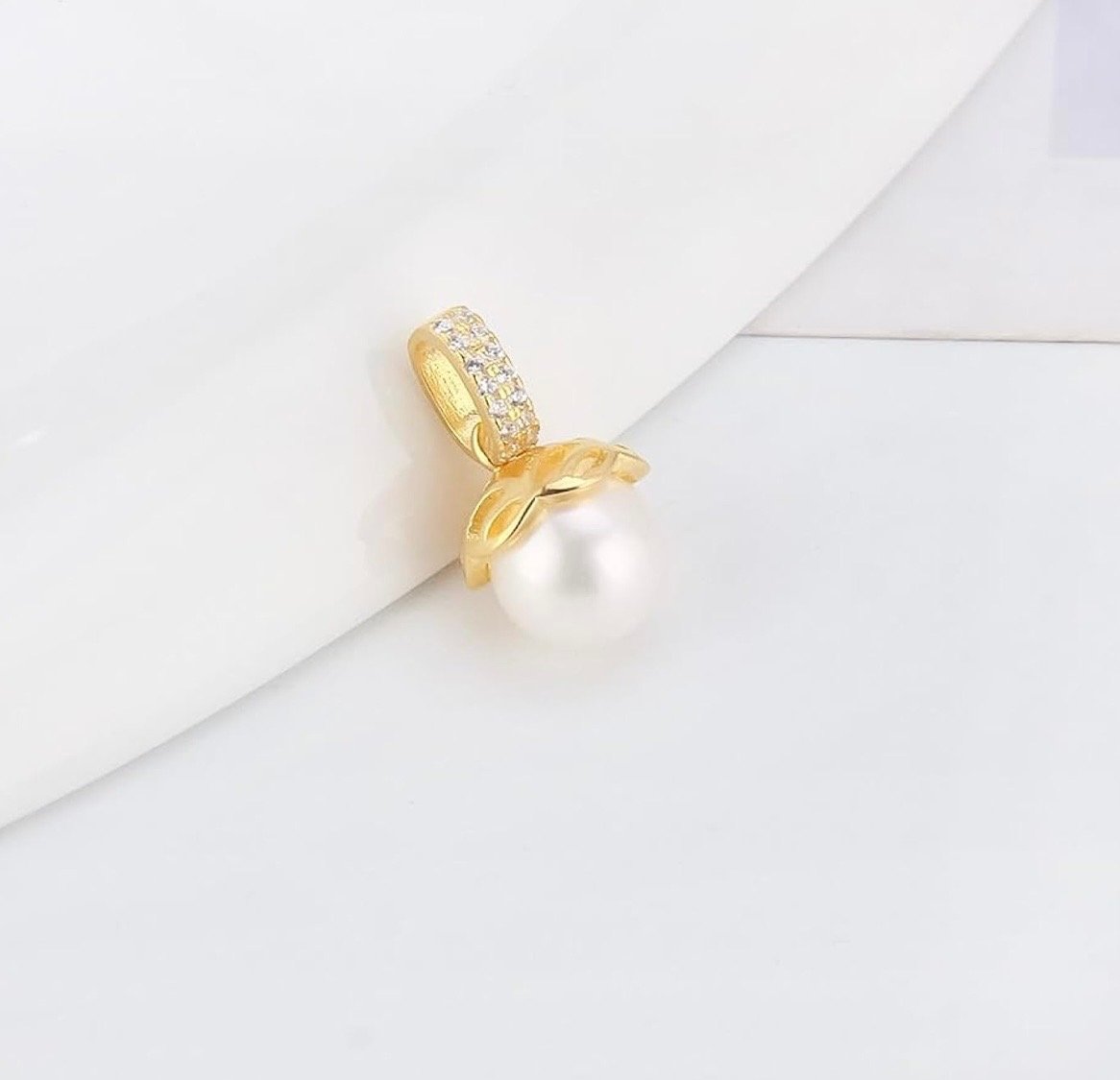 Gold pendant with a white pearl and small diamonds on the bail, resting on a white surface.